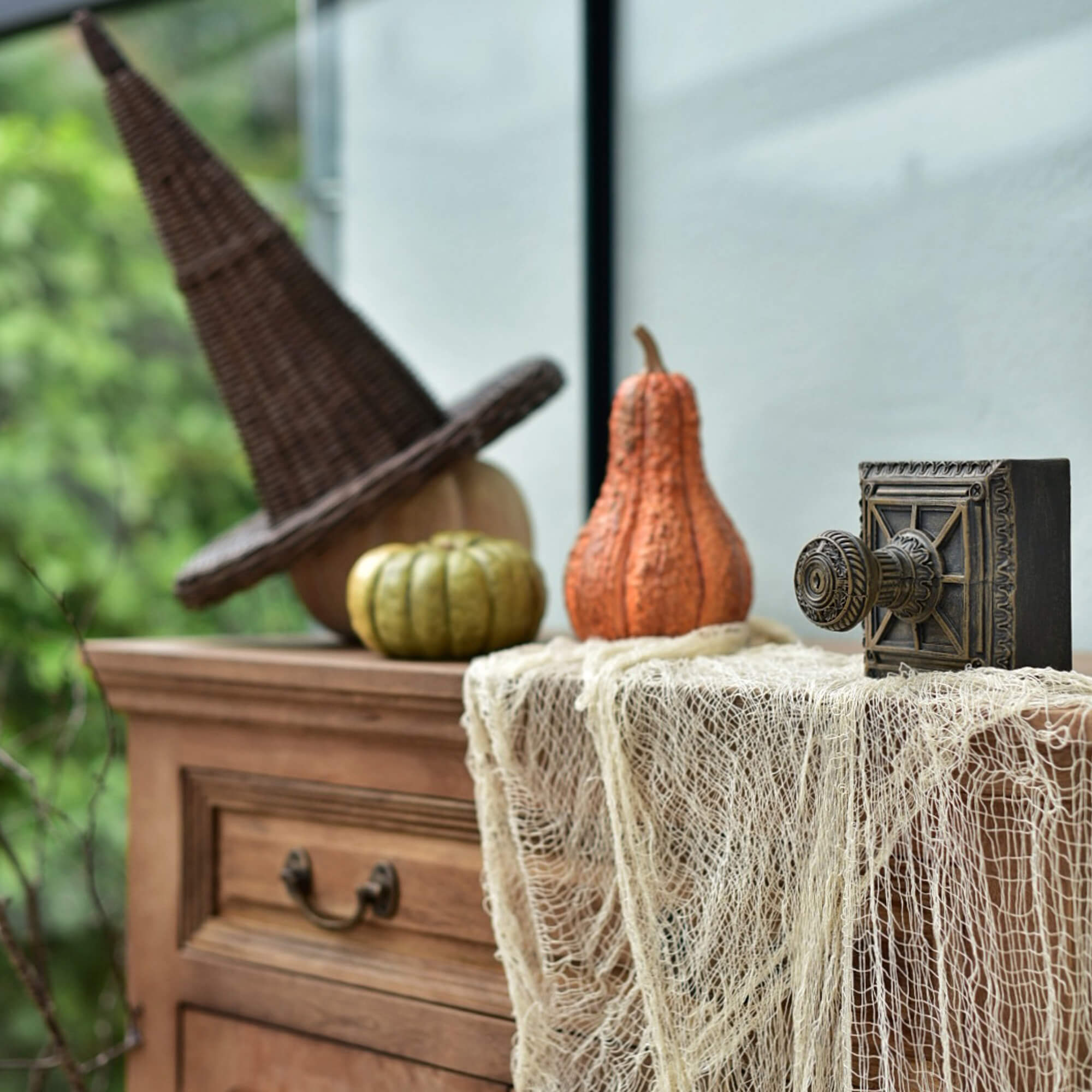 Holzkommode mit Hexenhut aus Korbgeflecht und Kürbissen als Halloween-Deko