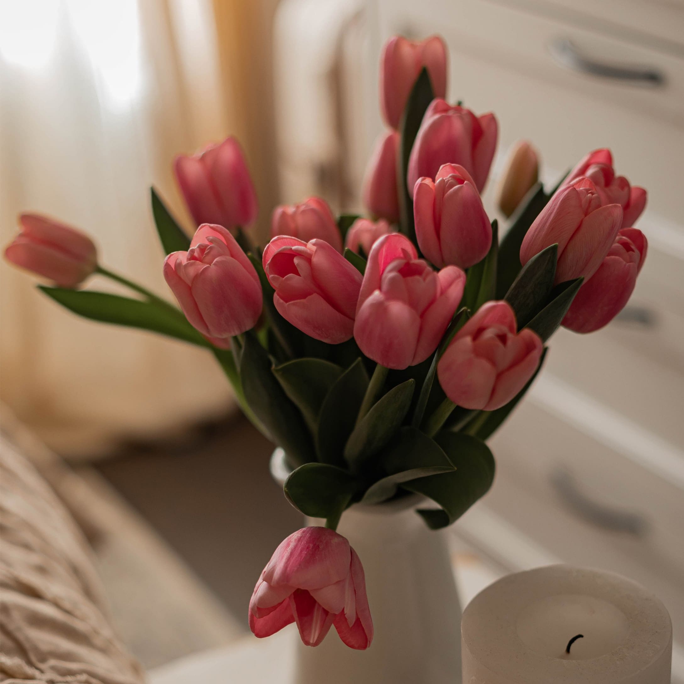 Strauß rosa Tulpen in weisser Vase vor hellem Schlafzimmerhintergrund