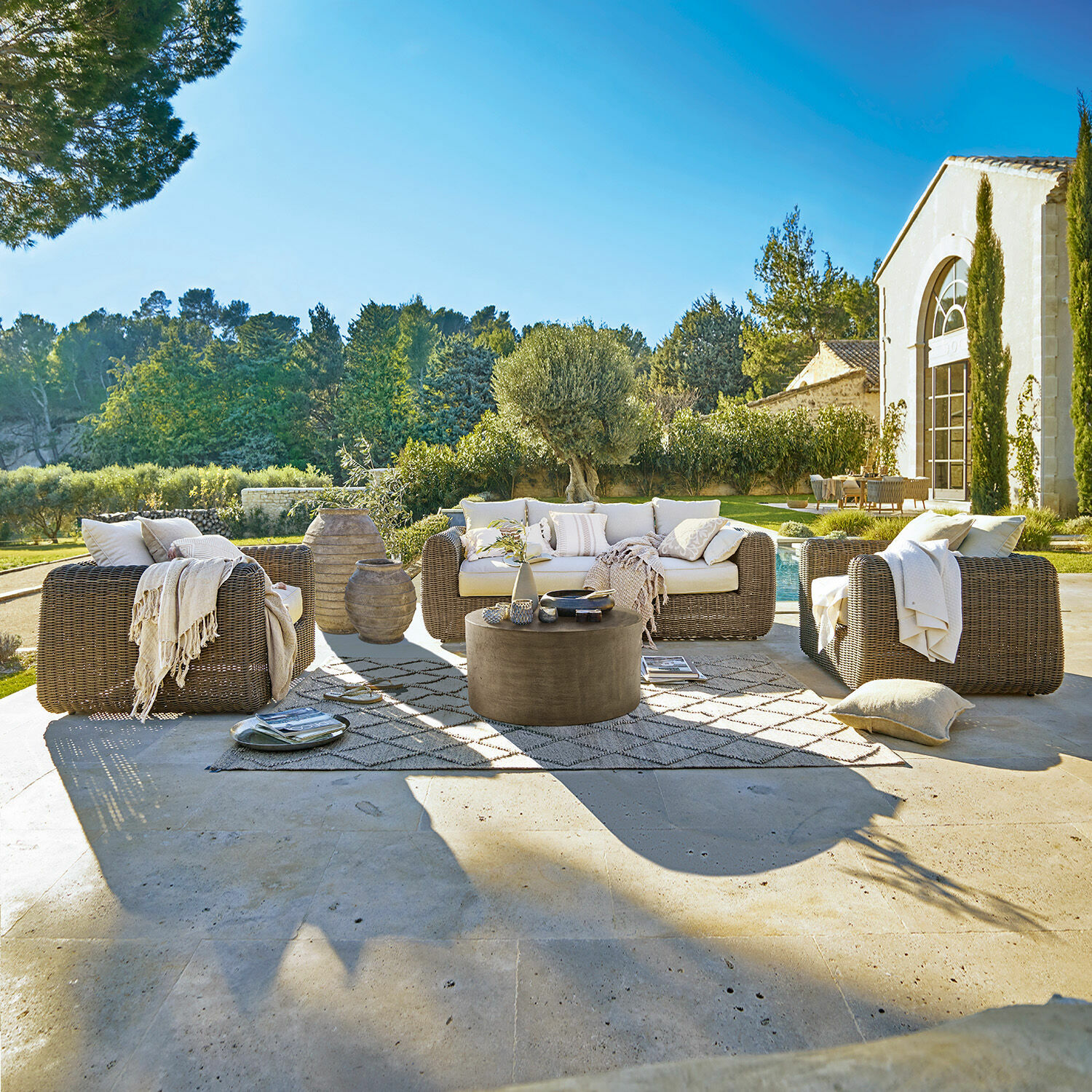 Sitzgruppe Bogdanne Braunes Rattan-Gartenmöbel-Set mit cremefarbenen Kissen auf Terrasse mit Blick auf den grünen Garten