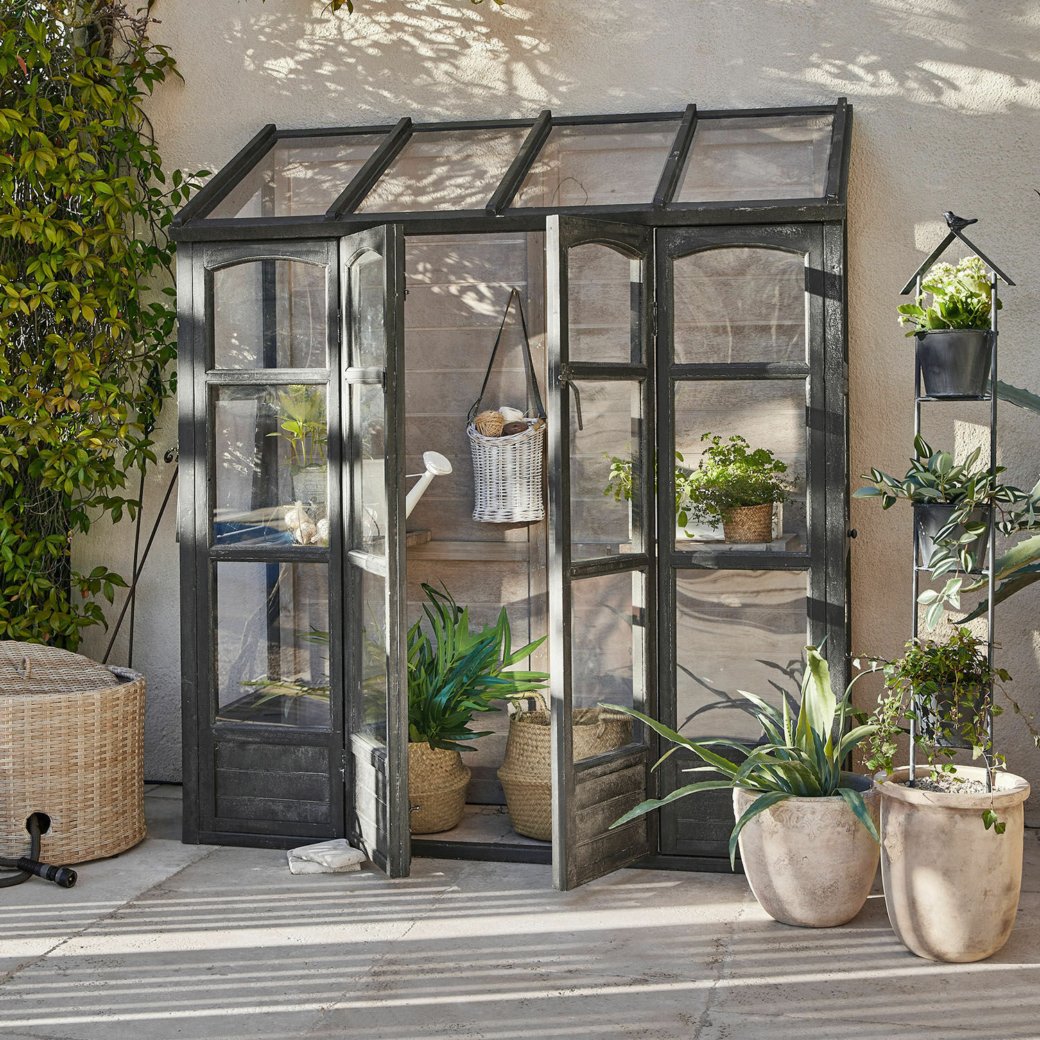 Gewächshaus Abilenne Kleines Gartengewächshaus mit schwarzem Metallrahmen und Pflanzen in Töpfen auf der Terrasse
