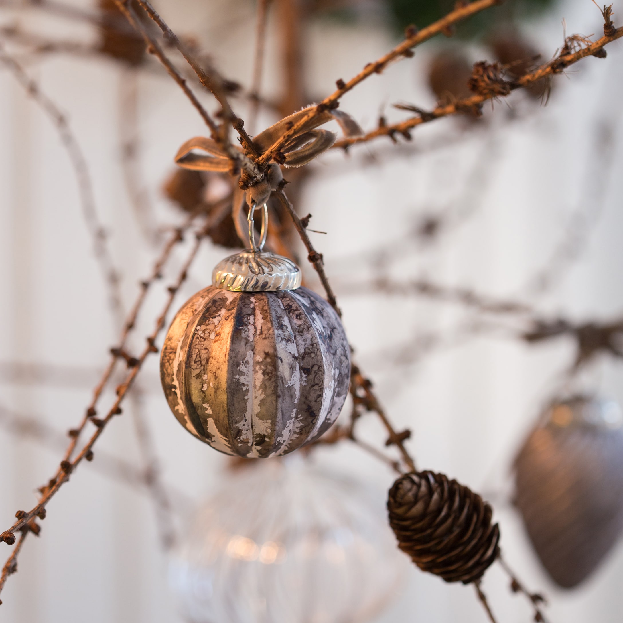 Glas-Weihnachtskugel in Braun-Grau an Zweig mit dekorativer Kiefernzapfen-Hängung