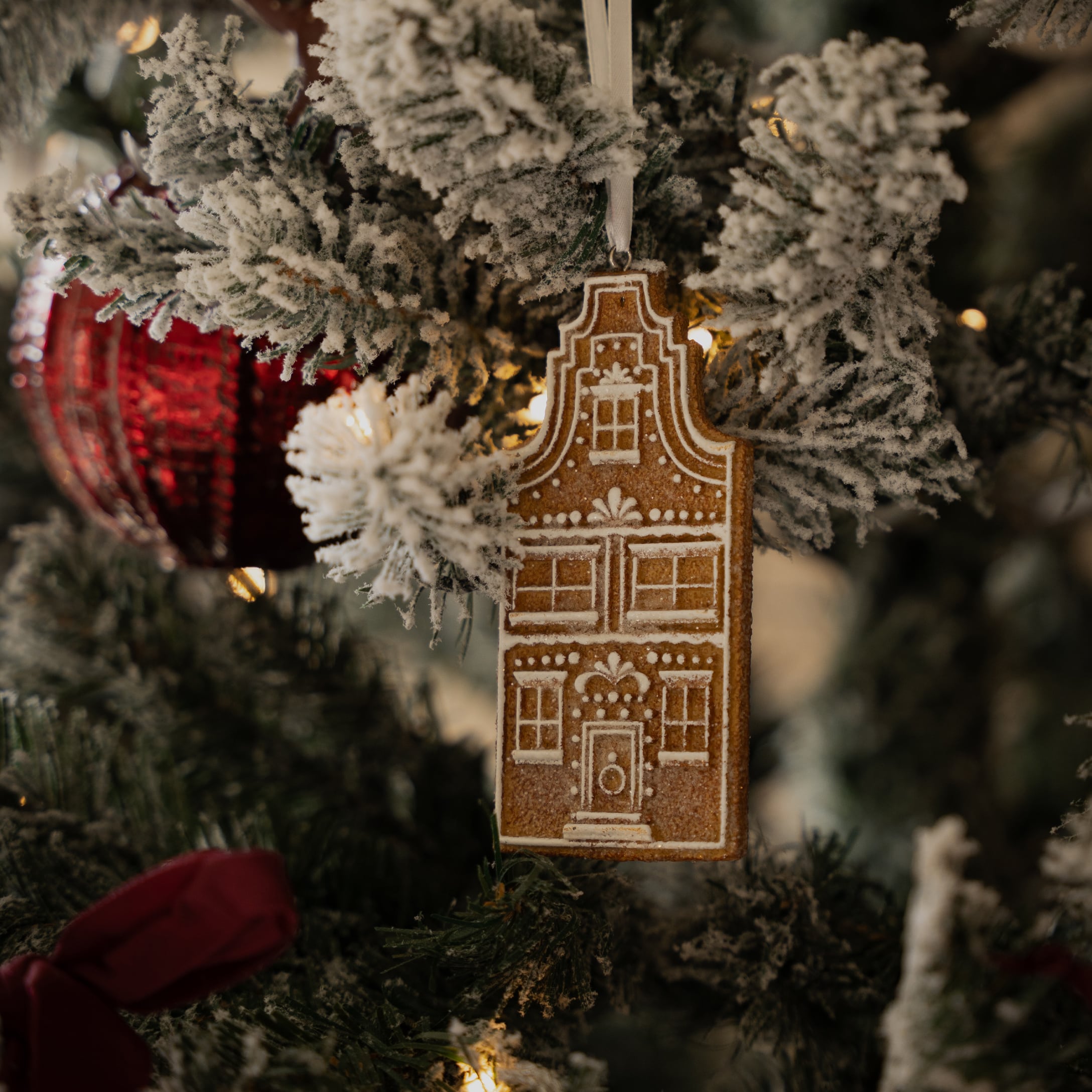Lebkuchen-Hausanhänger an schneebedecktem Tannenzweig mit rotem Christbaumschmuck