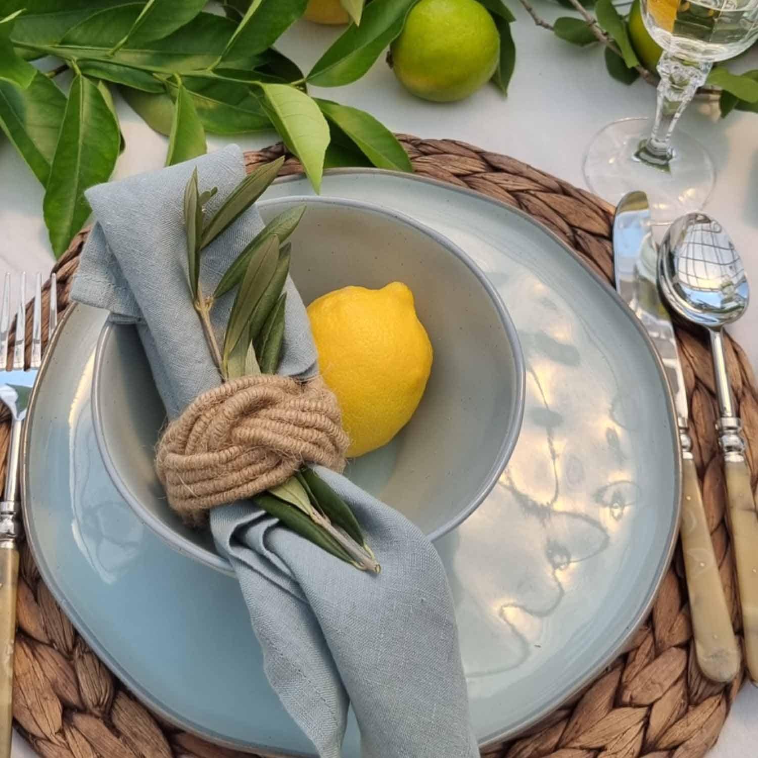 Blaues Keramikgeschirr mit Leinenserviette und Zitrone auf geflochtenem Tischset