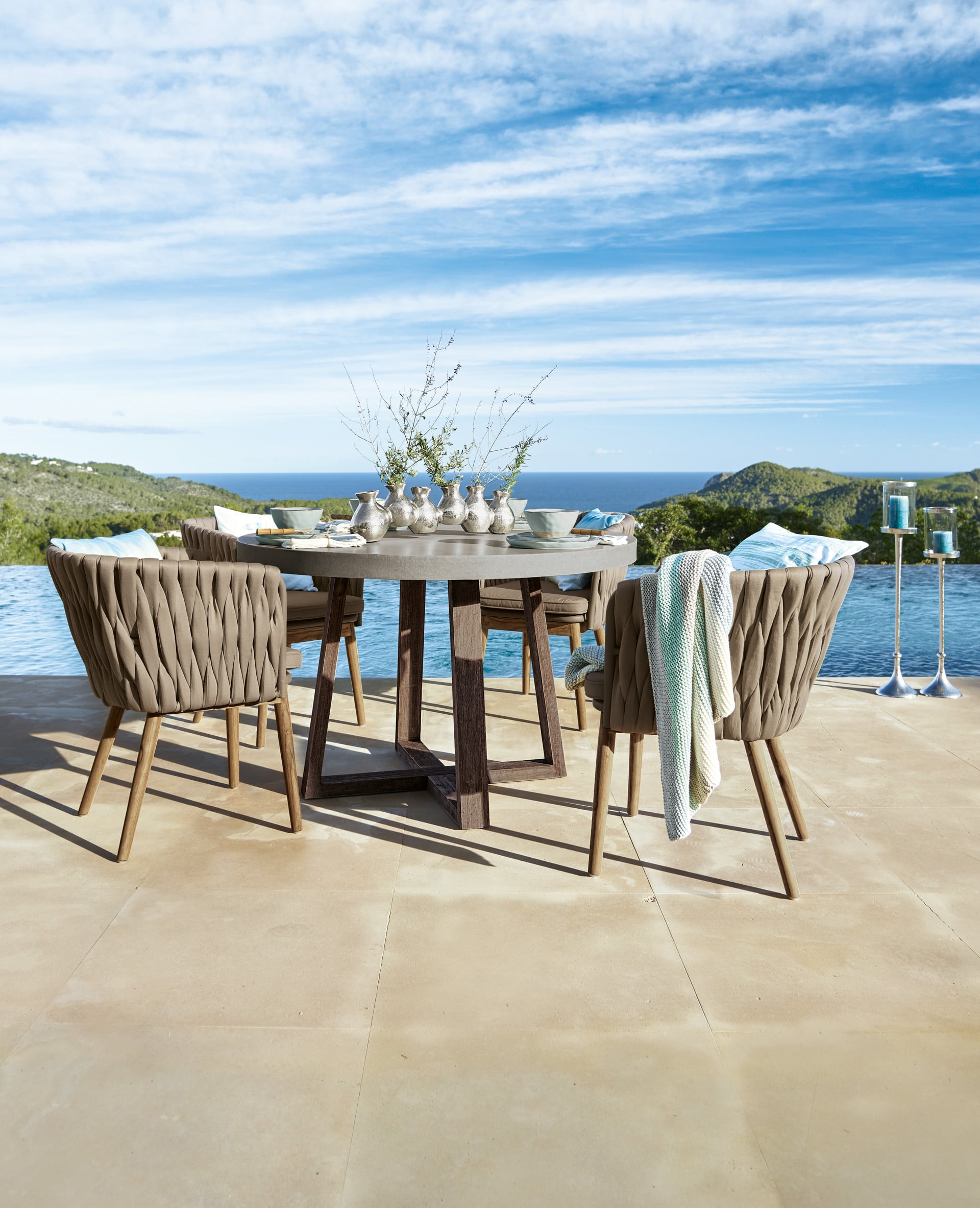 Gartenmöbel-Set mit rundem Tisch und braunen, geflochtenen Stühlen auf Terrasse mit Meerblick