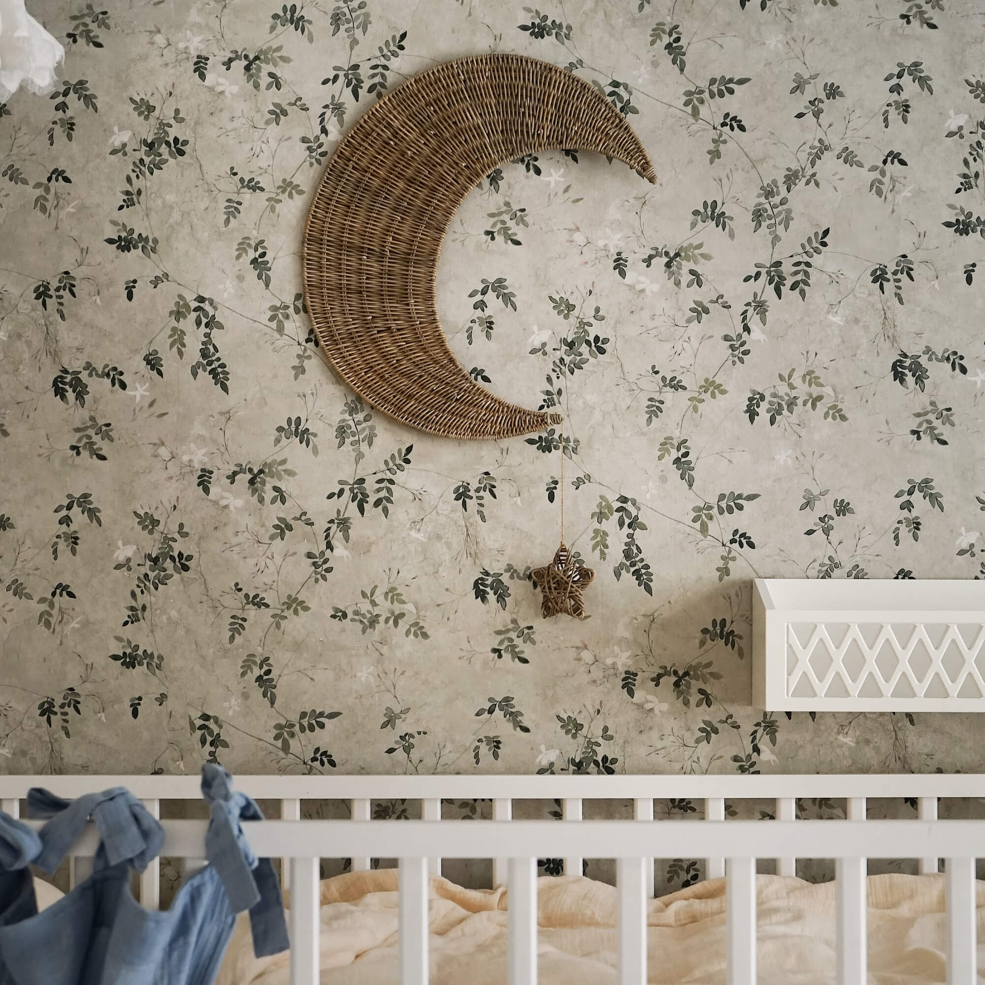 Wanddekoration Mond aus Rattan mit hängendem Stern vor floralem Tapetenmuster im Kinderzimmer