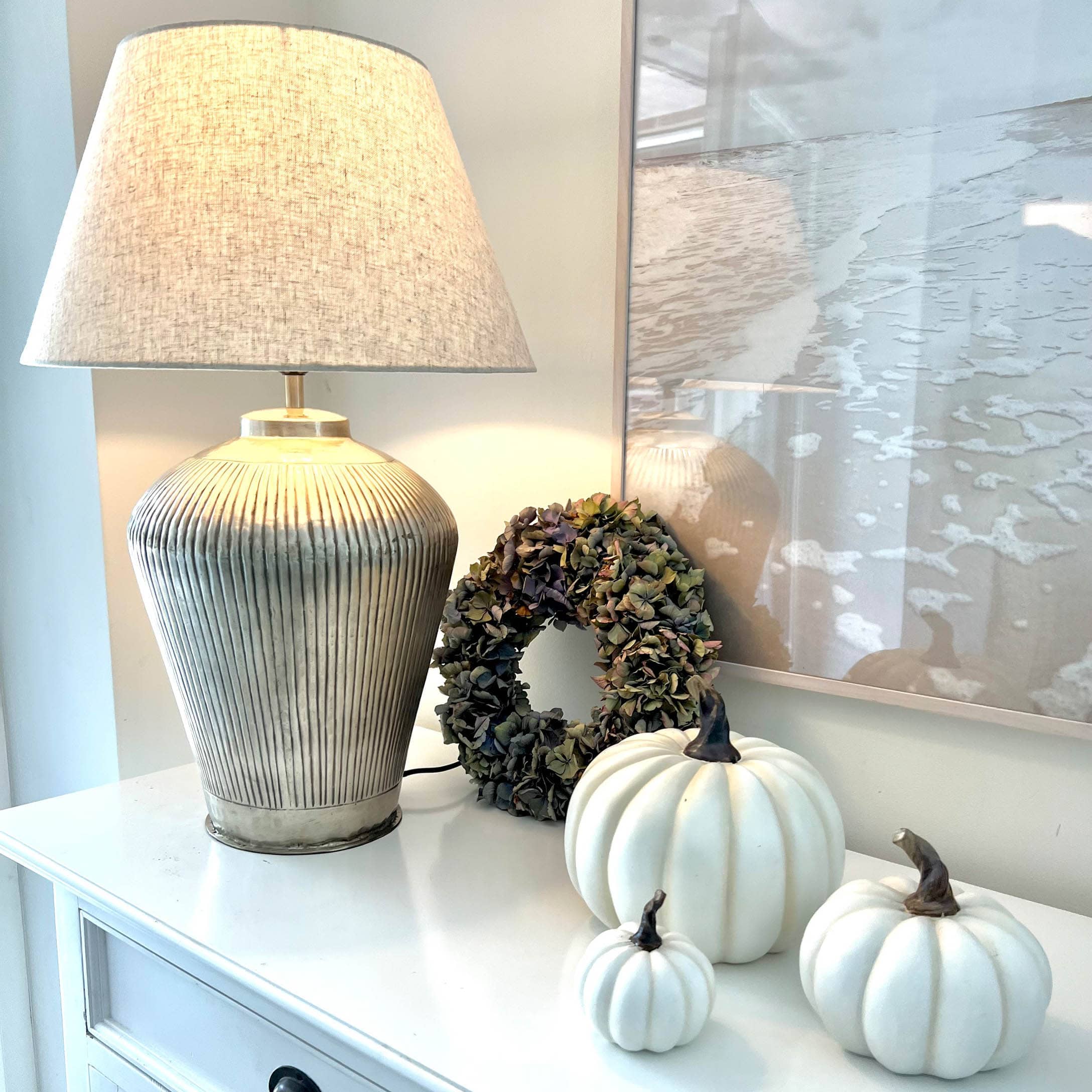 Tischlampe mit beigem Stoffschirm und Keramikfuss, weisse Dekokürbisse und getrockneter Blumenkranz