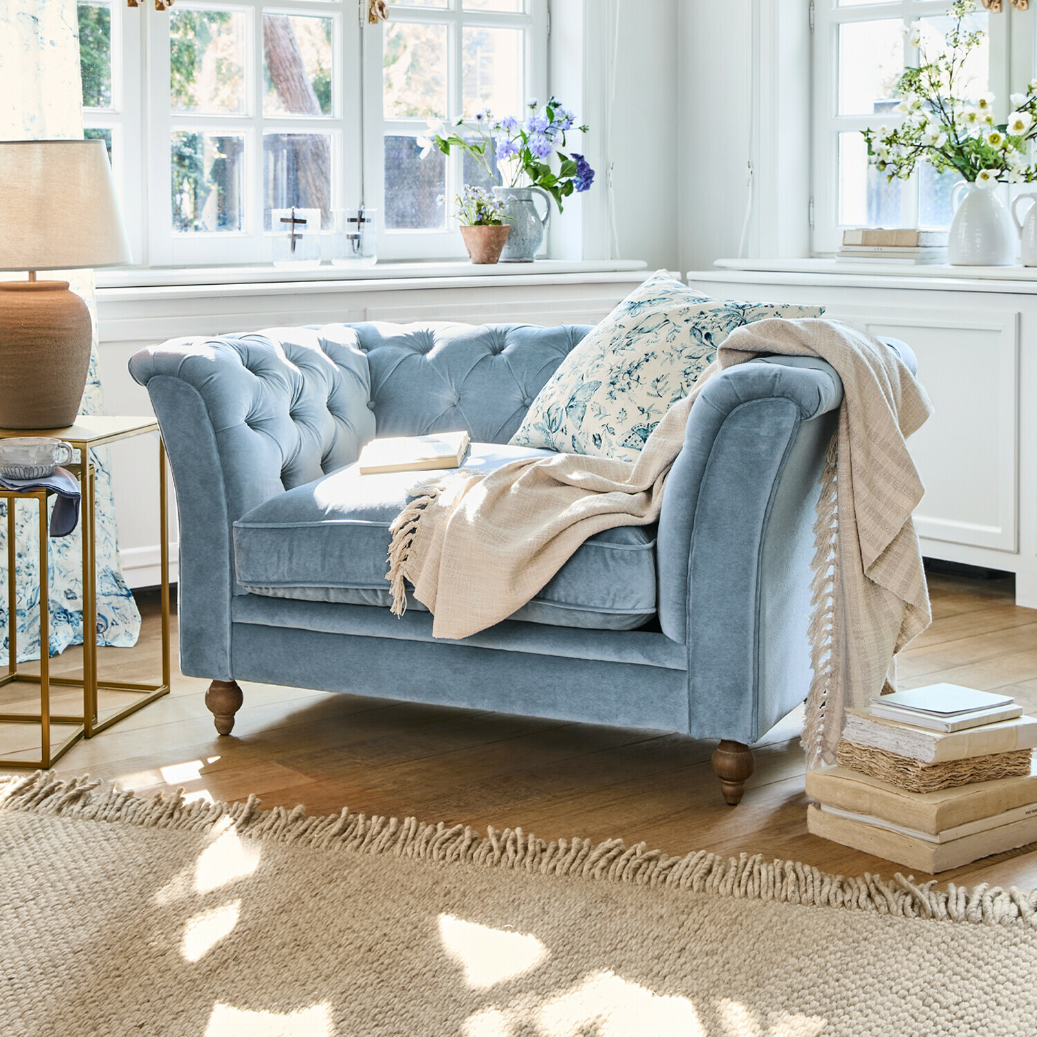 Sofa Clères Zweisitziges blaues Samtsofa mit gesteppter Rückenlehne und beiger Decke in hellem Wohnzimmer