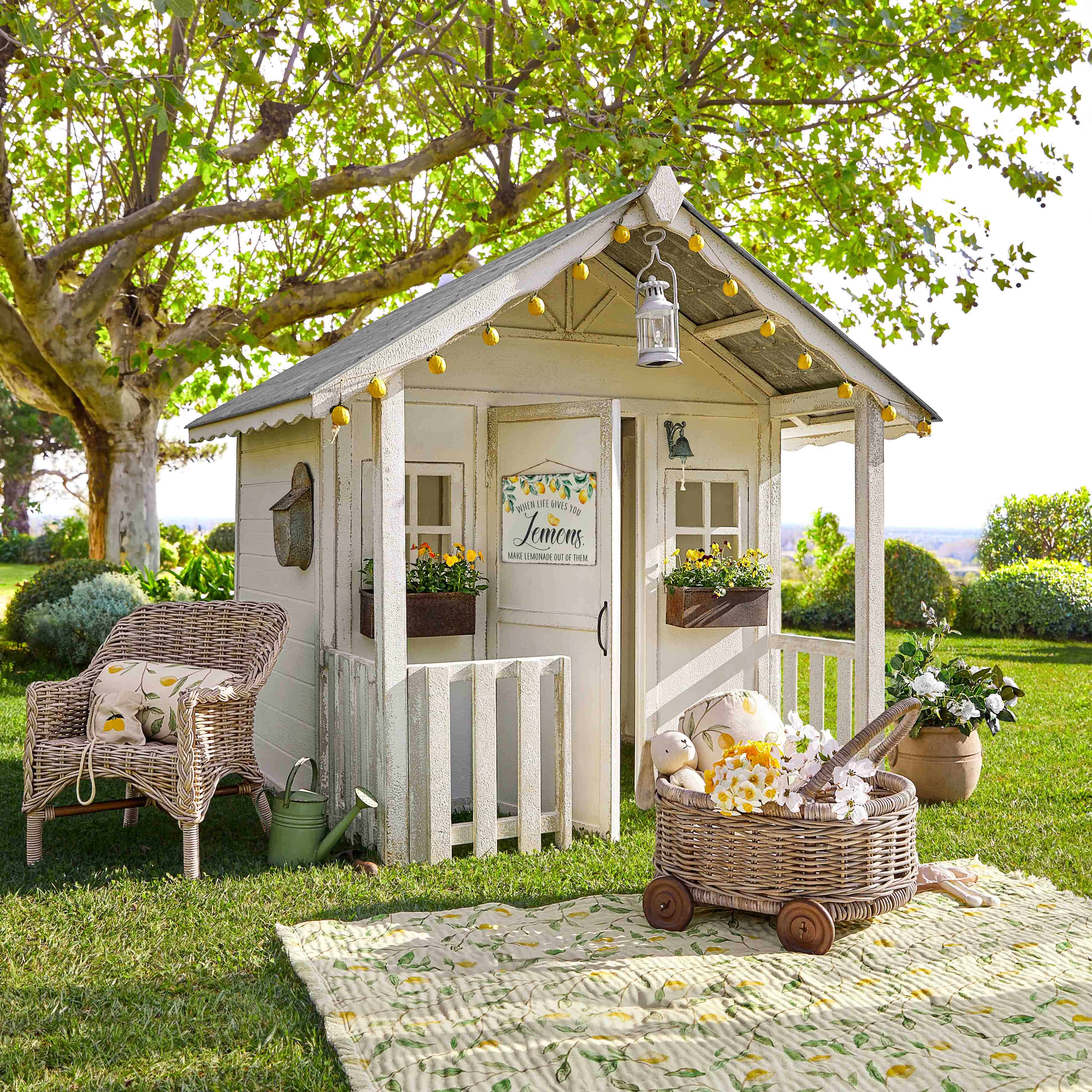 Weißes Holz-Gartenhaus mit Zitronendekoration und Korbsessel auf grünem Rasen im Garten