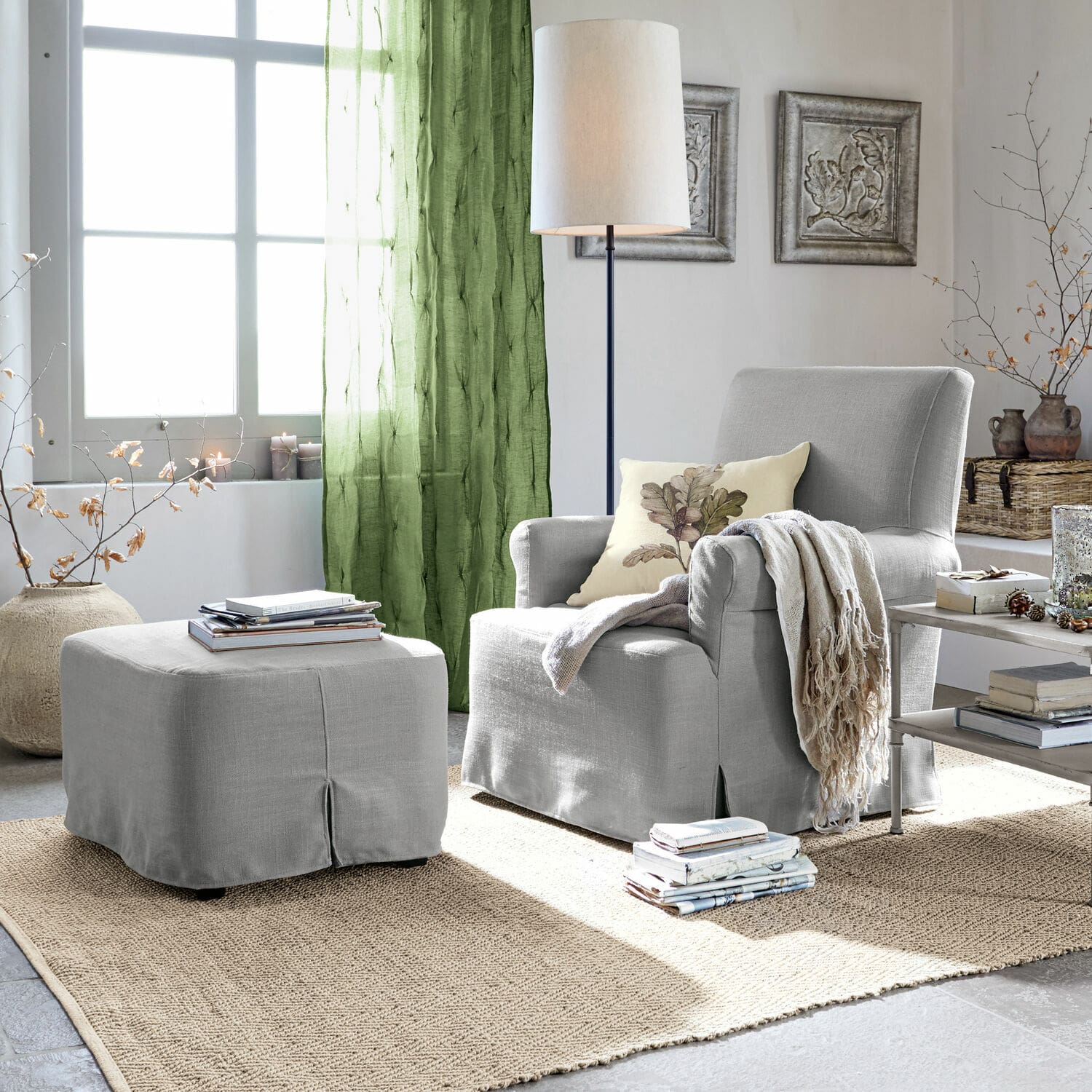 Grau bezogener Sessel mit Hocker und grünen Vorhängen in hellem Wohnzimmer mit Juteteppich.