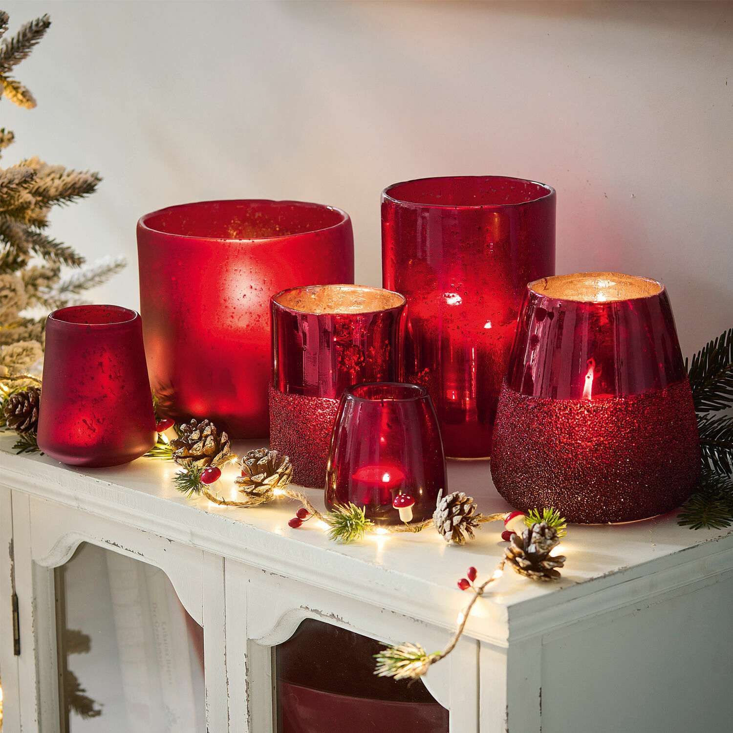Windlicht 6er Set Paro Set aus roten Glaswindlichtern in verschiedenen Formen auf weissem Schrank mit Weihnachtsdekoration