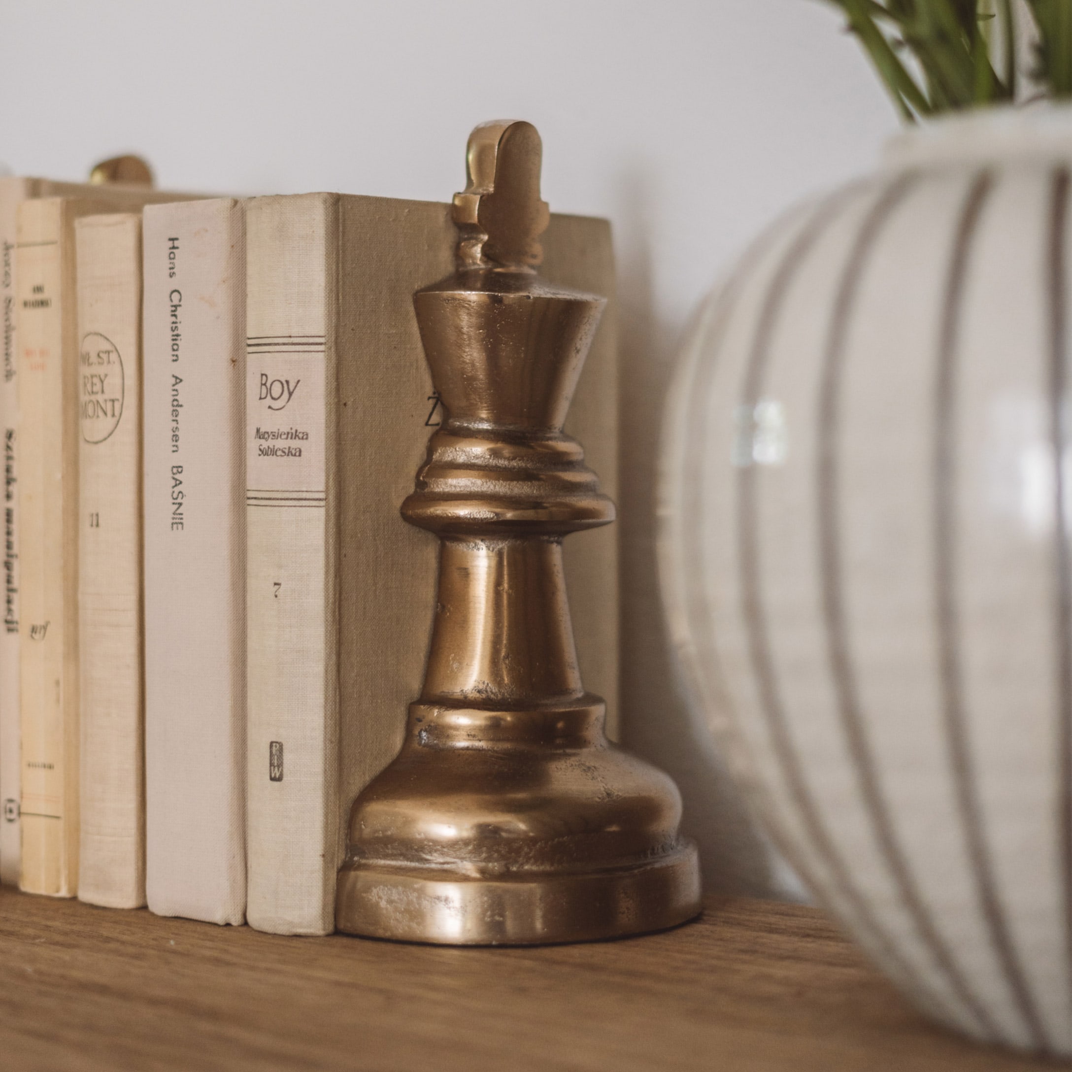 Goldfarbene Metall-Schachfigur als Dekoration auf Holzregal neben Büchern