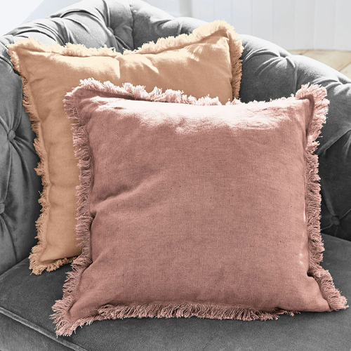 Zwei dekorative Leinenkissen in Rosa und Beige mit Fransen auf grauem Sofa, gemütliche Atmosphäre