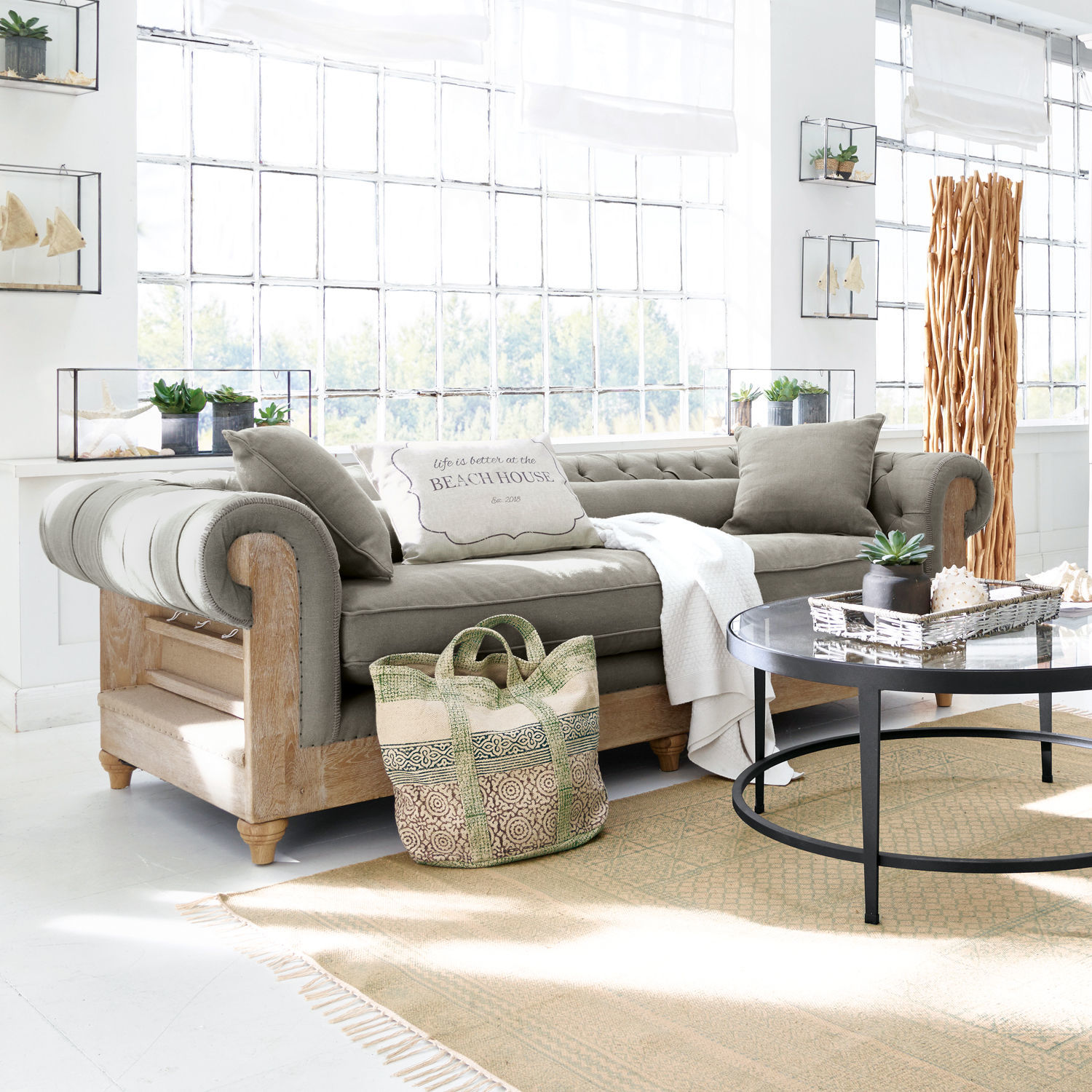 Sofa Kanani Graues Sofa mit Holzrahmen im hellen Wohnzimmer mit Dekorationen und grossem Fenster