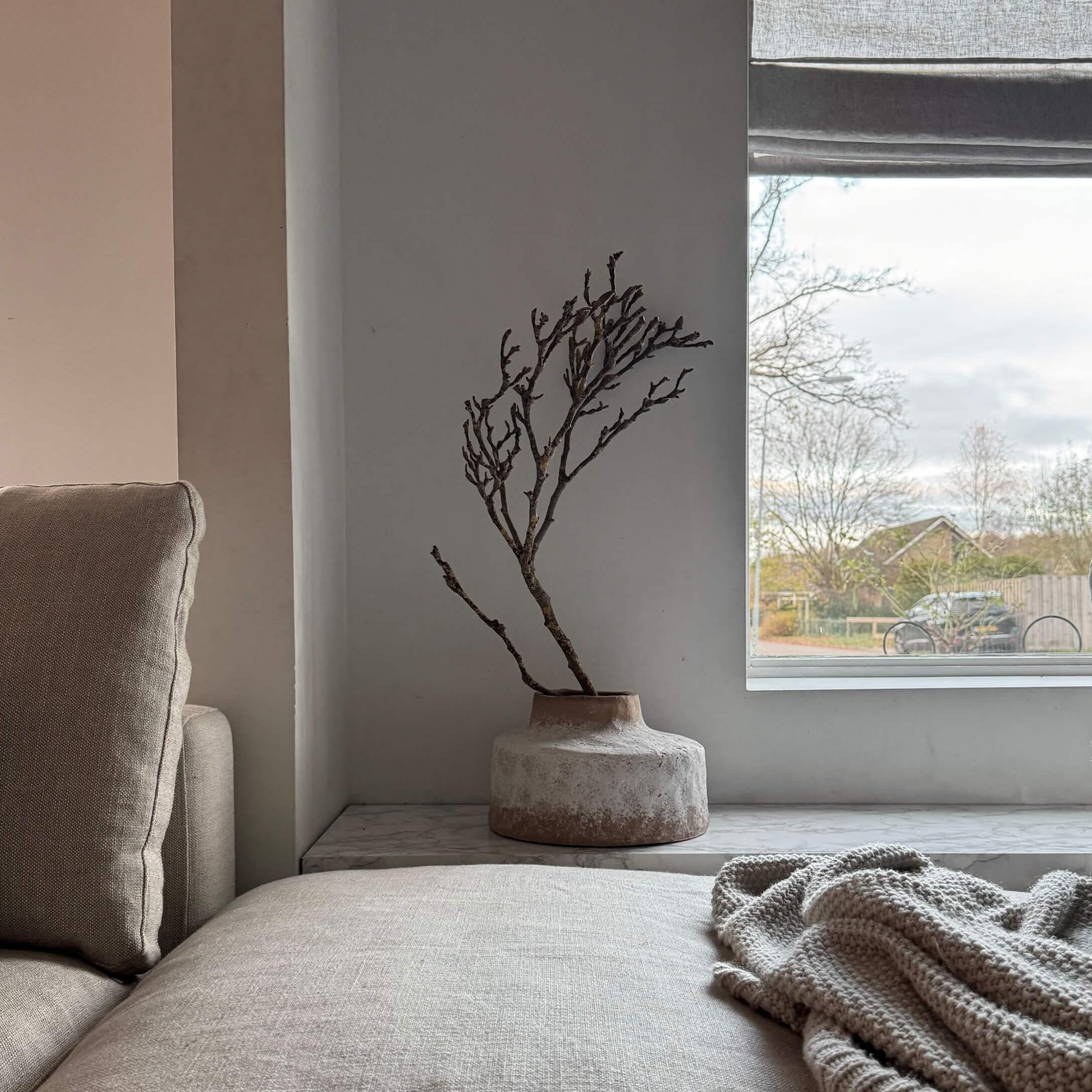 Beige Keramikvase mit trockenem Zweig auf Fensterbank in hellem Wohnzimmer