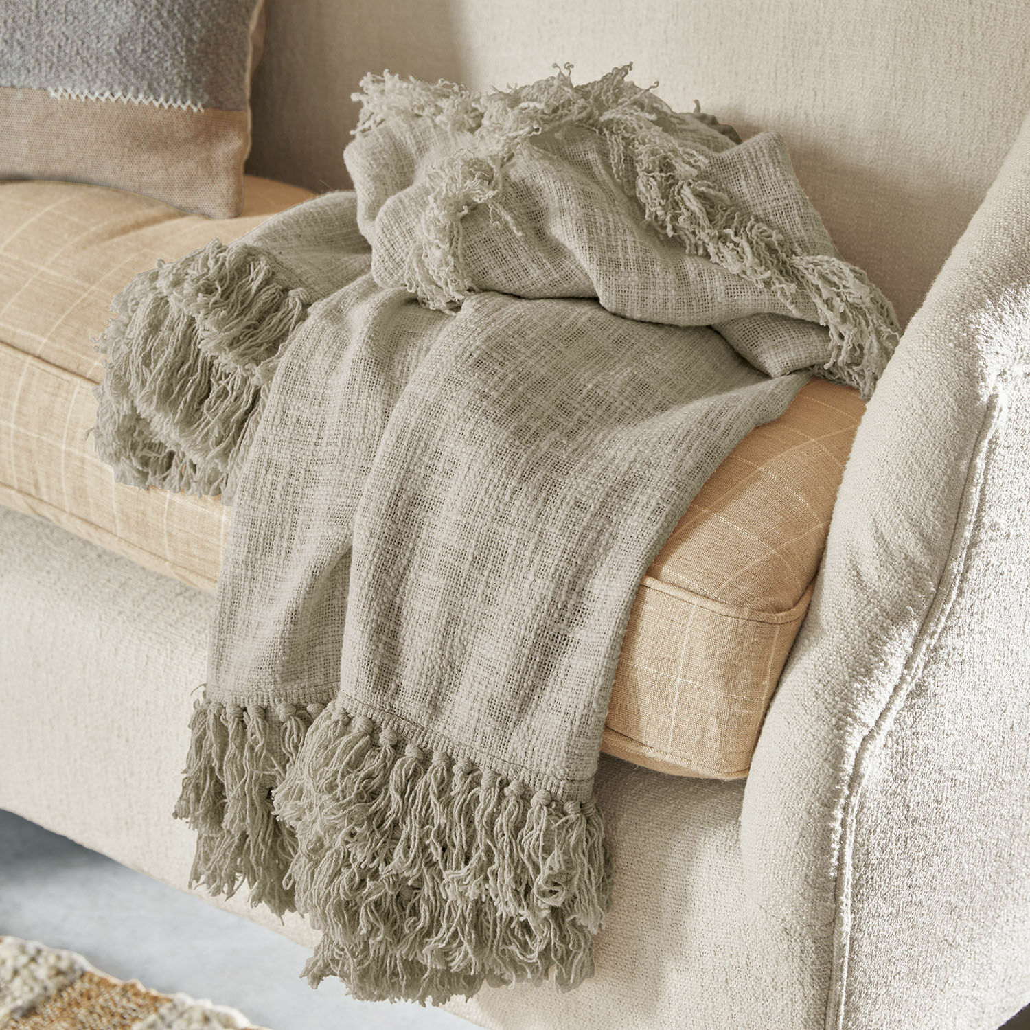 Plaid Freya Beige Fransendecke aus weichem Material auf hellem Sofa, gemütliche Wohnraumdekoration