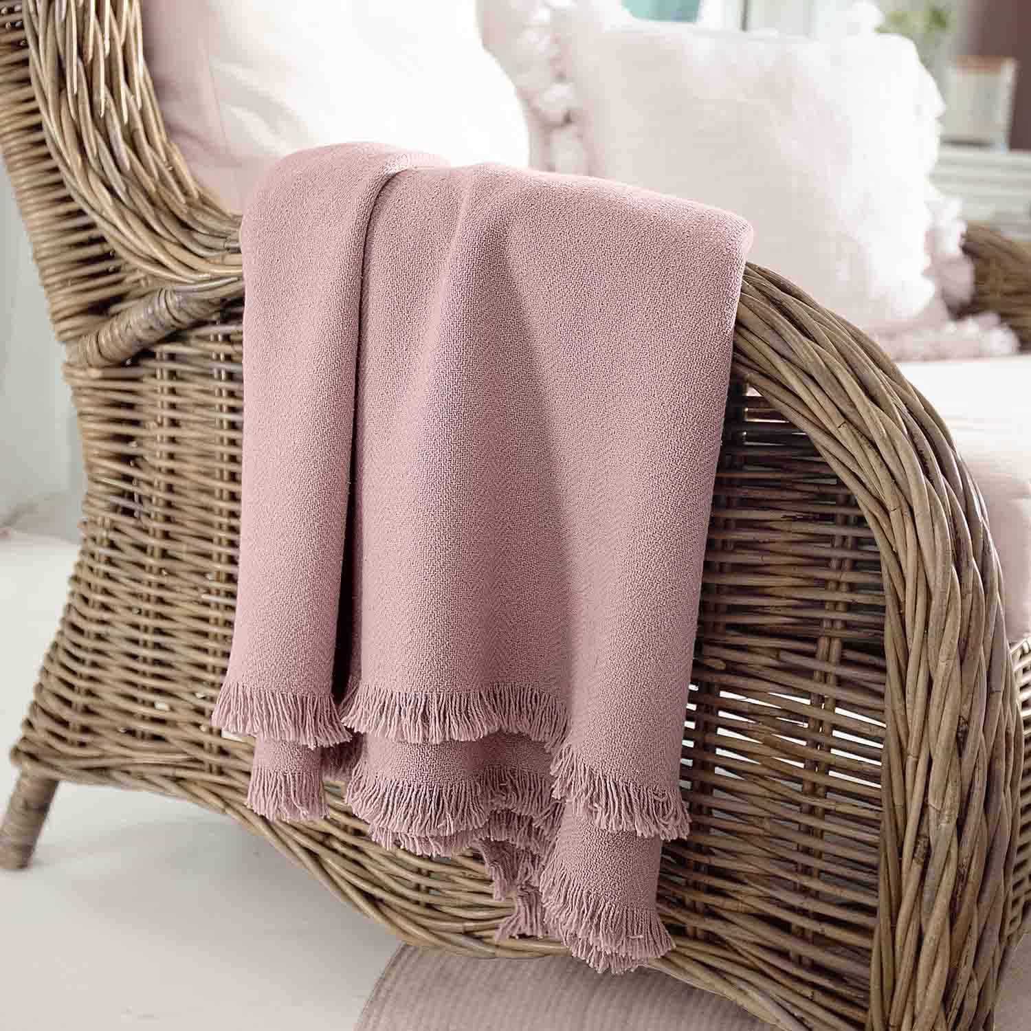 Rosa Decke aus weichem Stoff mit Fransen auf Rattansessel, gemütliche Wohnraumdekoration