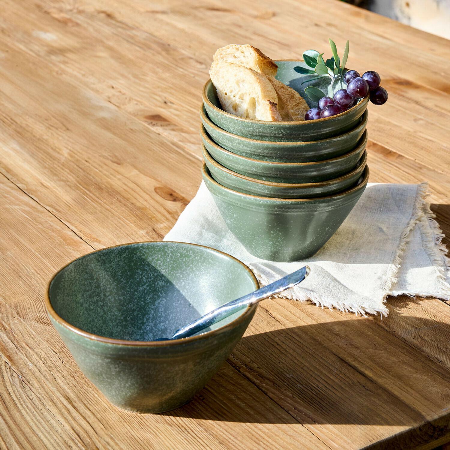 Grünes Keramikschalen-Set auf Holztisch mit Brot und Trauben für die Küche