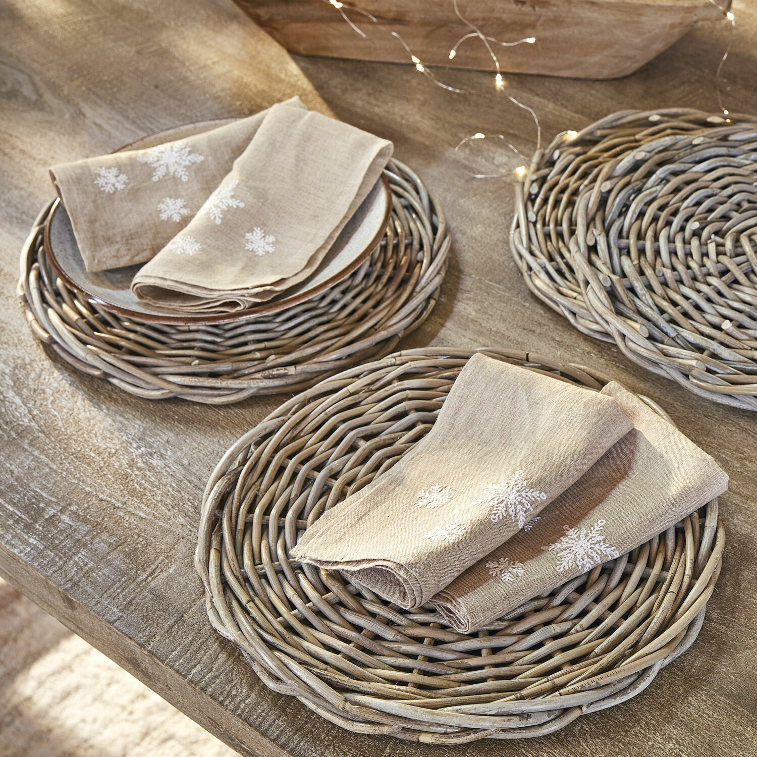 Serviette 4er Set Ruspi Beige Leinenservietten mit Schneeflockenstickerei auf geflochtenen Weidenuntersetzern auf Holztisch