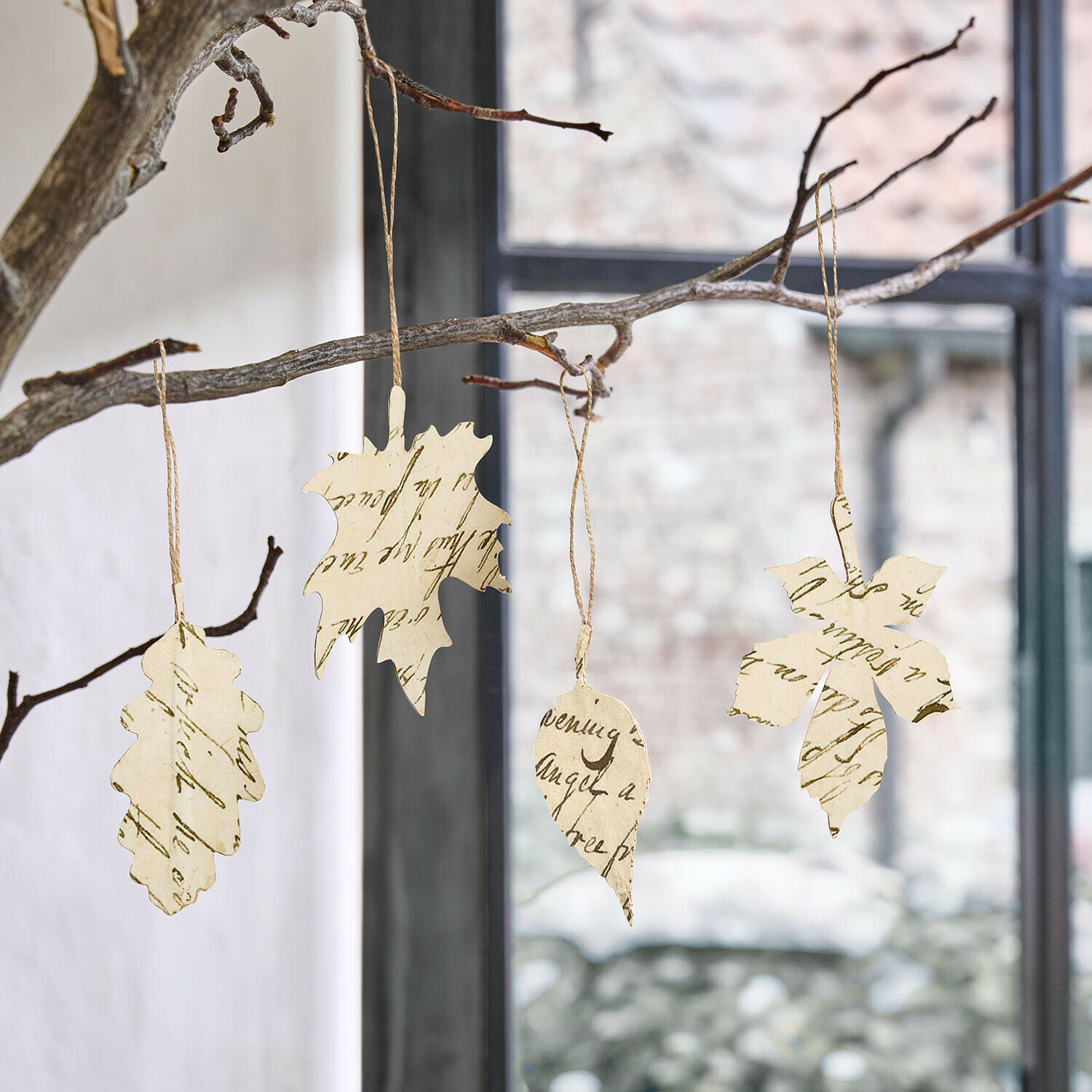 Anhänger 4er Set Fleuriene Papierblätter mit Schrift als Dekoration an Zweigen hängend vor Fenster