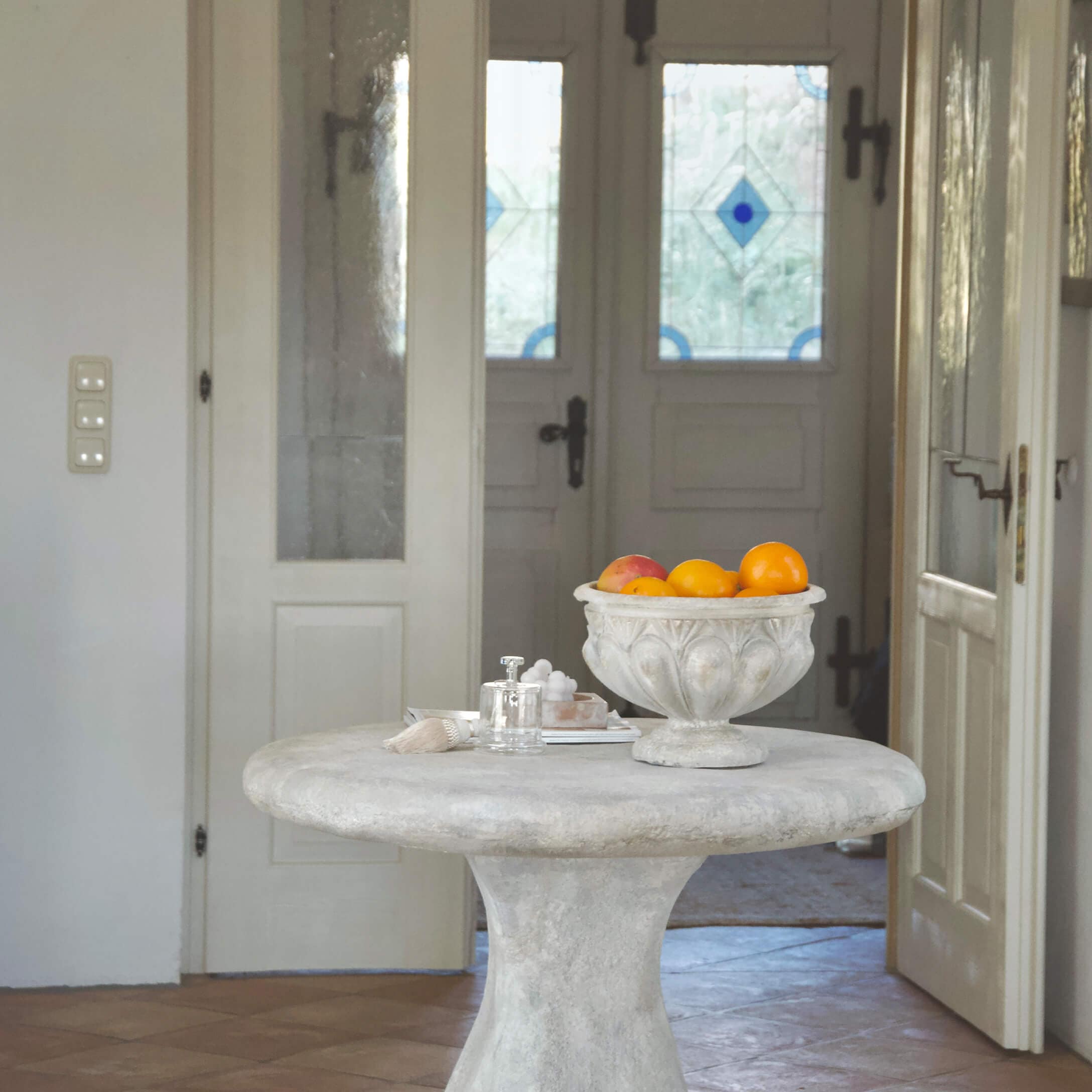 Runder Tisch aus hellem Beton mit dekorativer Vintage-Schale voller Orangen