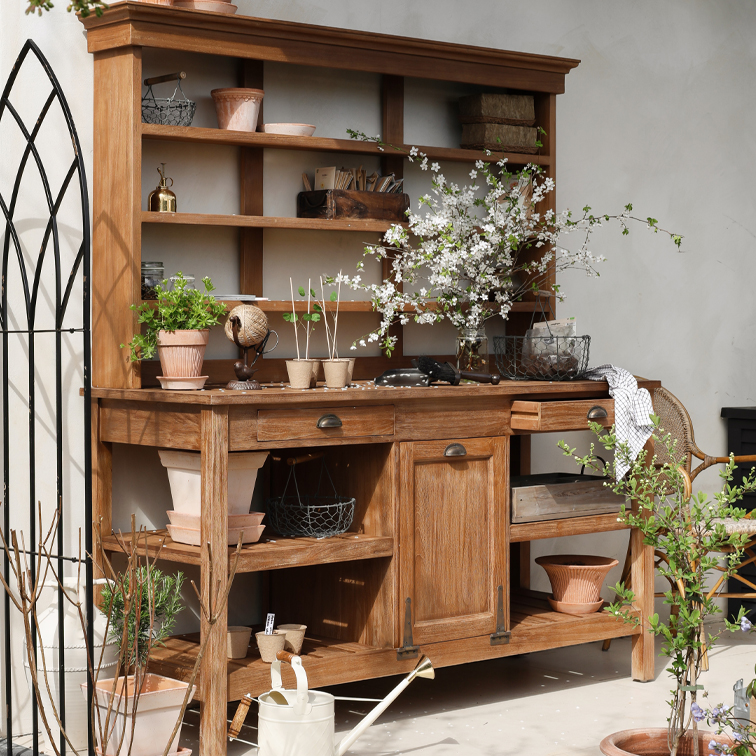 Holz-Gartenschrank mit Regalen, Blumentöpfen und blühenden Zweigen, dekoriert mit Gartengeräten.