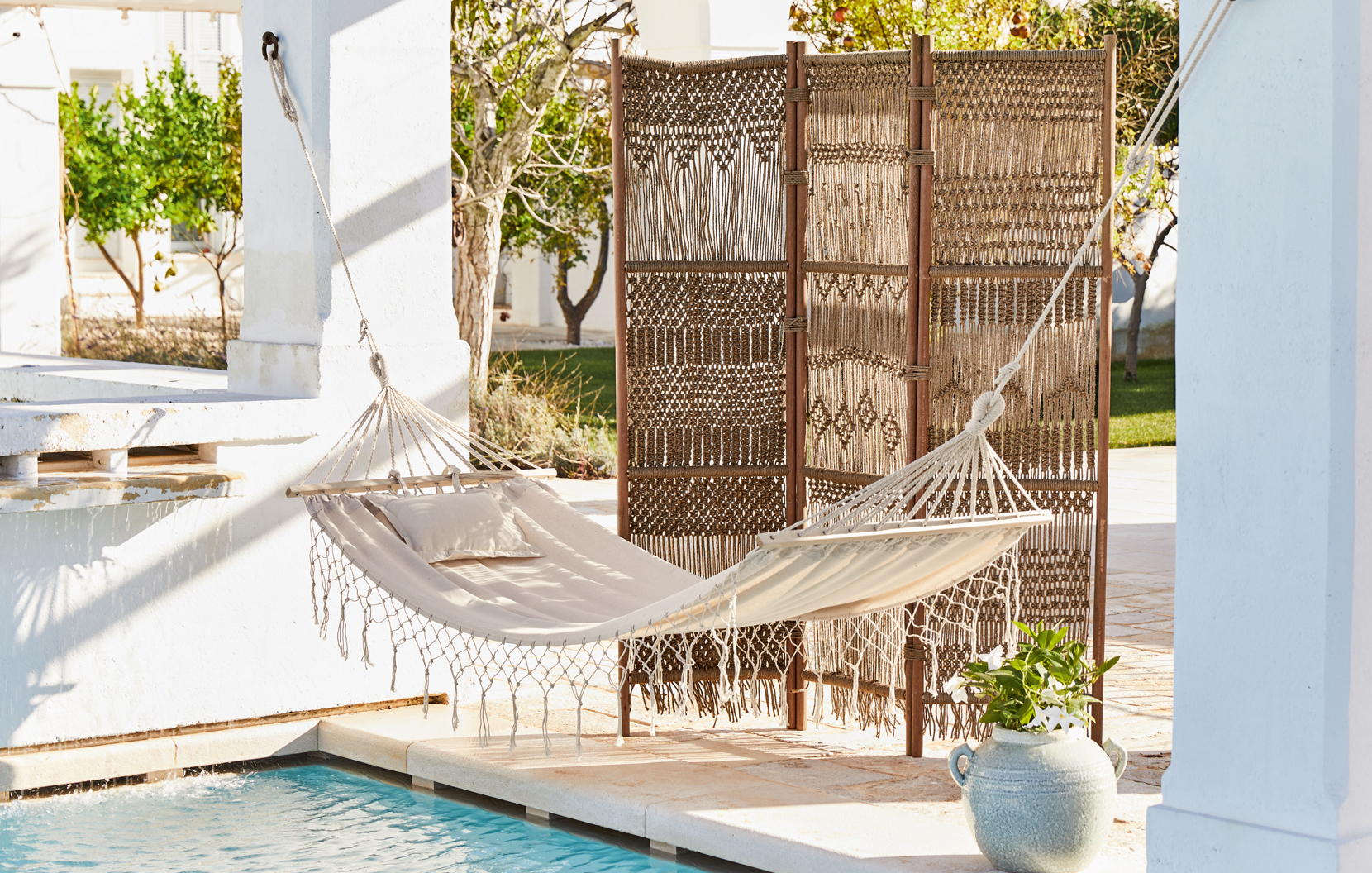 Beige Stoffhängematte mit Kissen und geflochtenem Paravent auf der Terrasse beim Pool im Boho-Stil