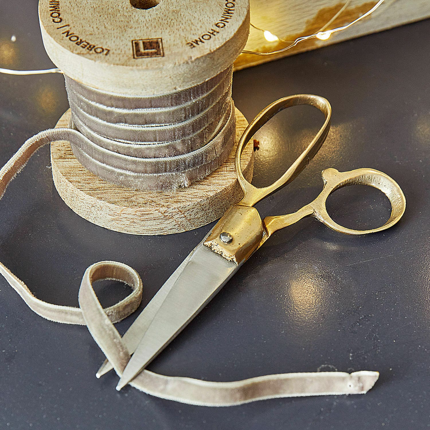 Schere Sterre Goldene Schere und beiges Samtband auf Holzspule auf dunklem Tisch zur Dekoration und zum Nähen