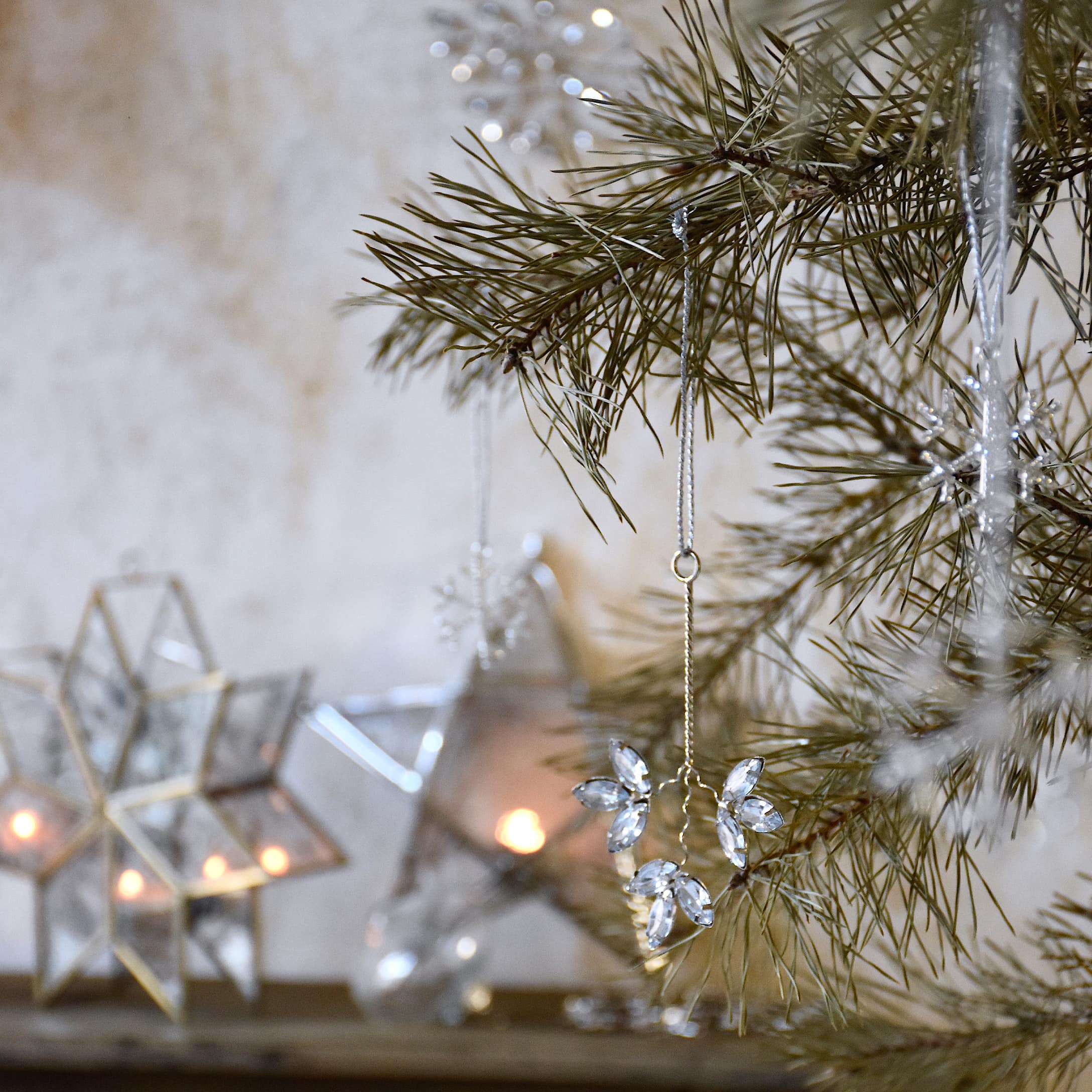 Weihnachtsdekoration mit Kristallanhängern an einem Kieferzweig und leuchtenden Sternen im Hintergrund