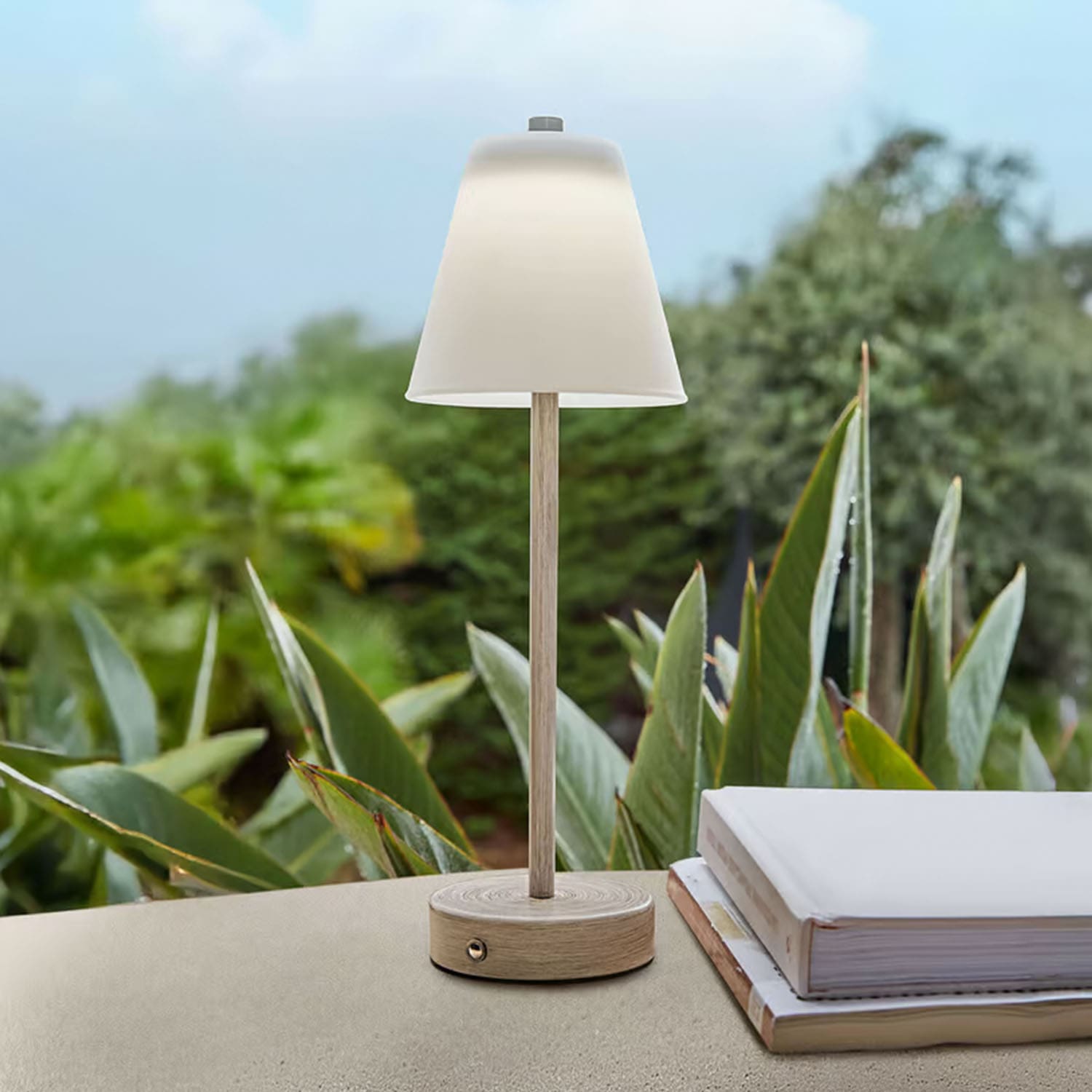 Tischlampe aus hellem Holz mit weissem Lampenschirm vor grünen Pflanzen, Wohnaccessoire