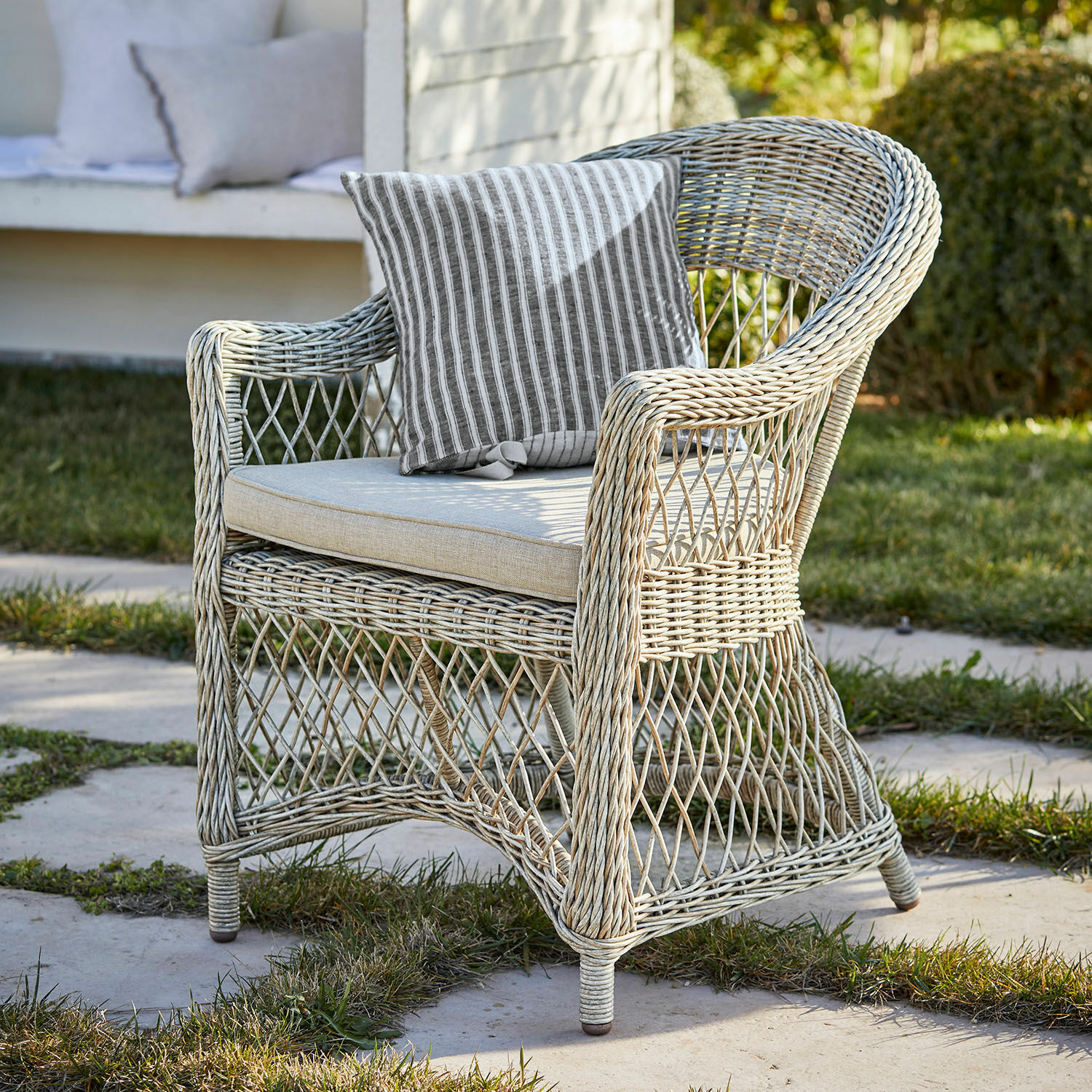 Sessel Lézardrieux Heller Rattan-Gartenstuhl mit gestreiftem Kissen, ideal für entspannte Momente im Freien.