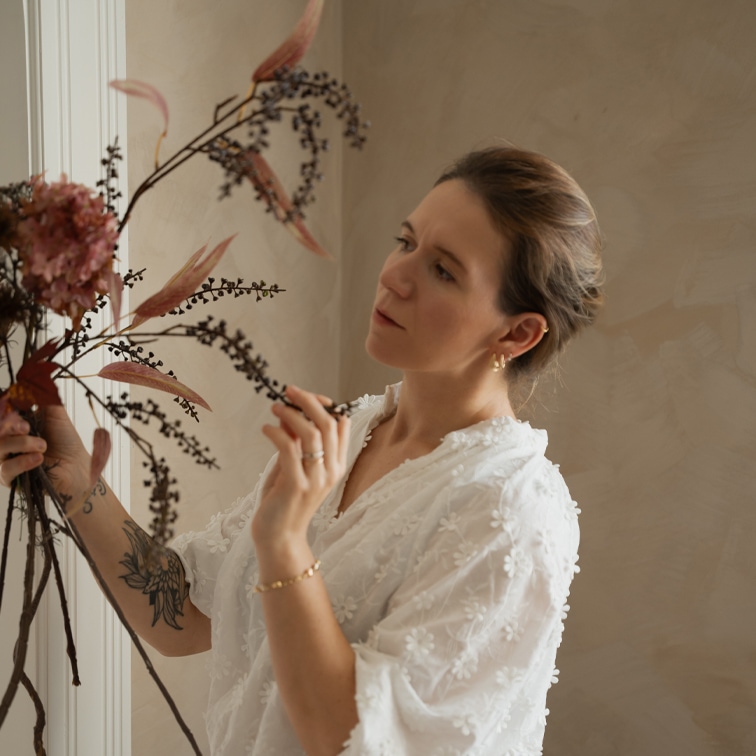 Frau in weisser Spitzenbluse arrangiert getrocknete Blumendekoration in hellem Raum