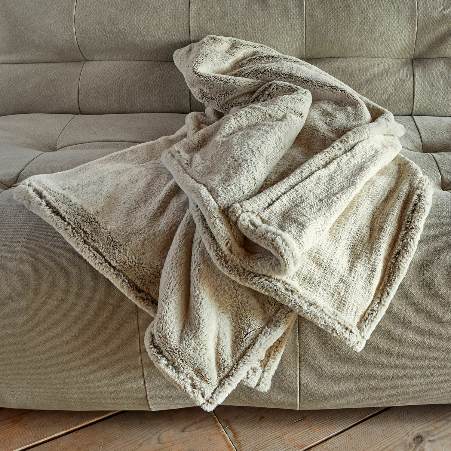 Plaid Newman Weiche, cremefarbene Kuscheldecke mit Fellbesatz auf beigem Sofa für gemütliche Wohnräume