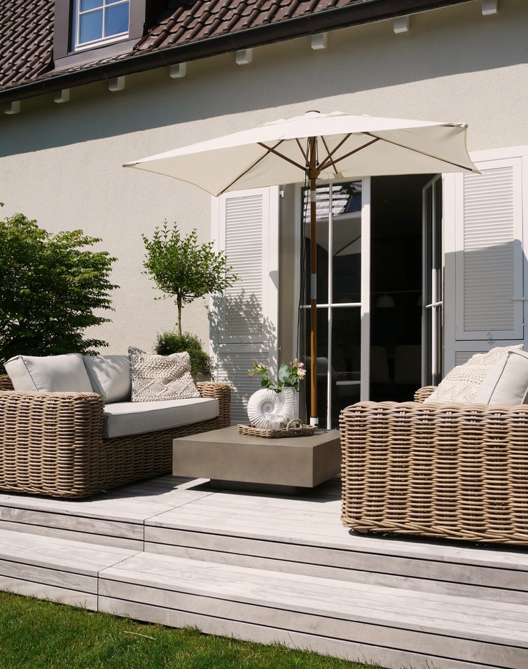 Modernes Gartenmöbel-Set aus beigem Rattan mit Sonnenschirm und Kissen auf hellem Holzdeck