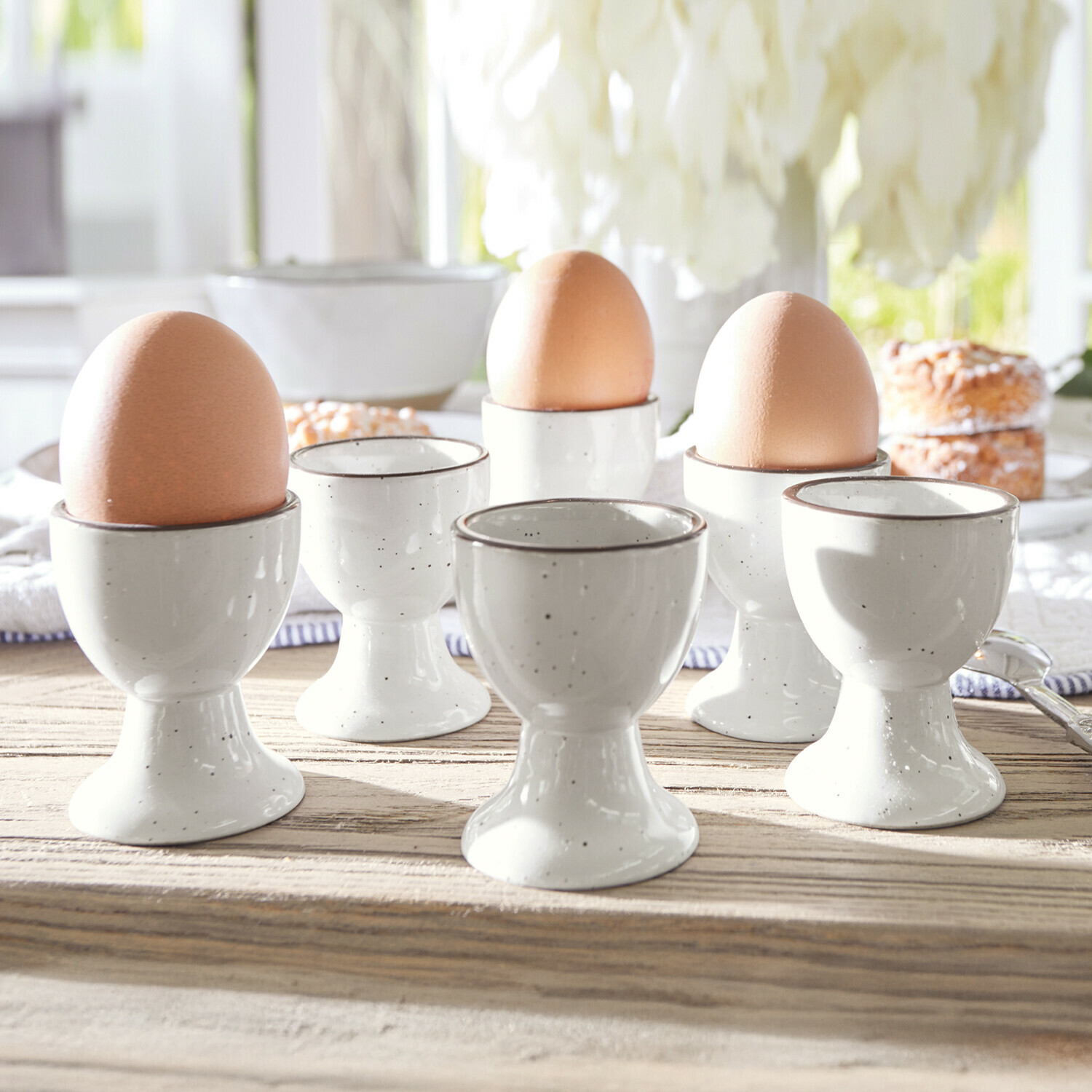 Eierbecher 6er Set Biarré Set aus weissen Keramik-Eierbechern mit braunen Eiern auf hellem Holztisch