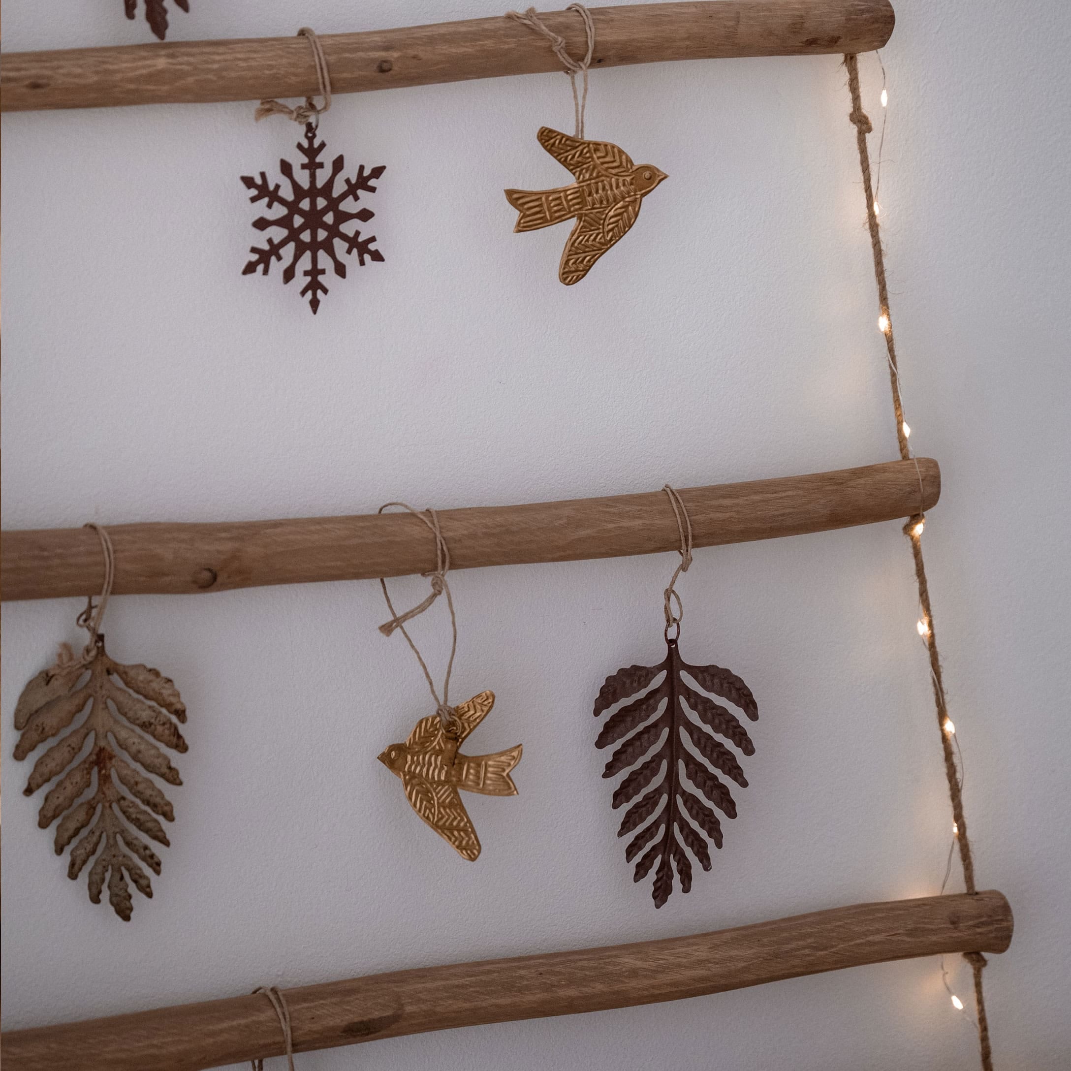 Metall-Weihnachtsschmuck in Form von Blättern, Vögeln und Schneeflocken, an einer Holzleiter hängend