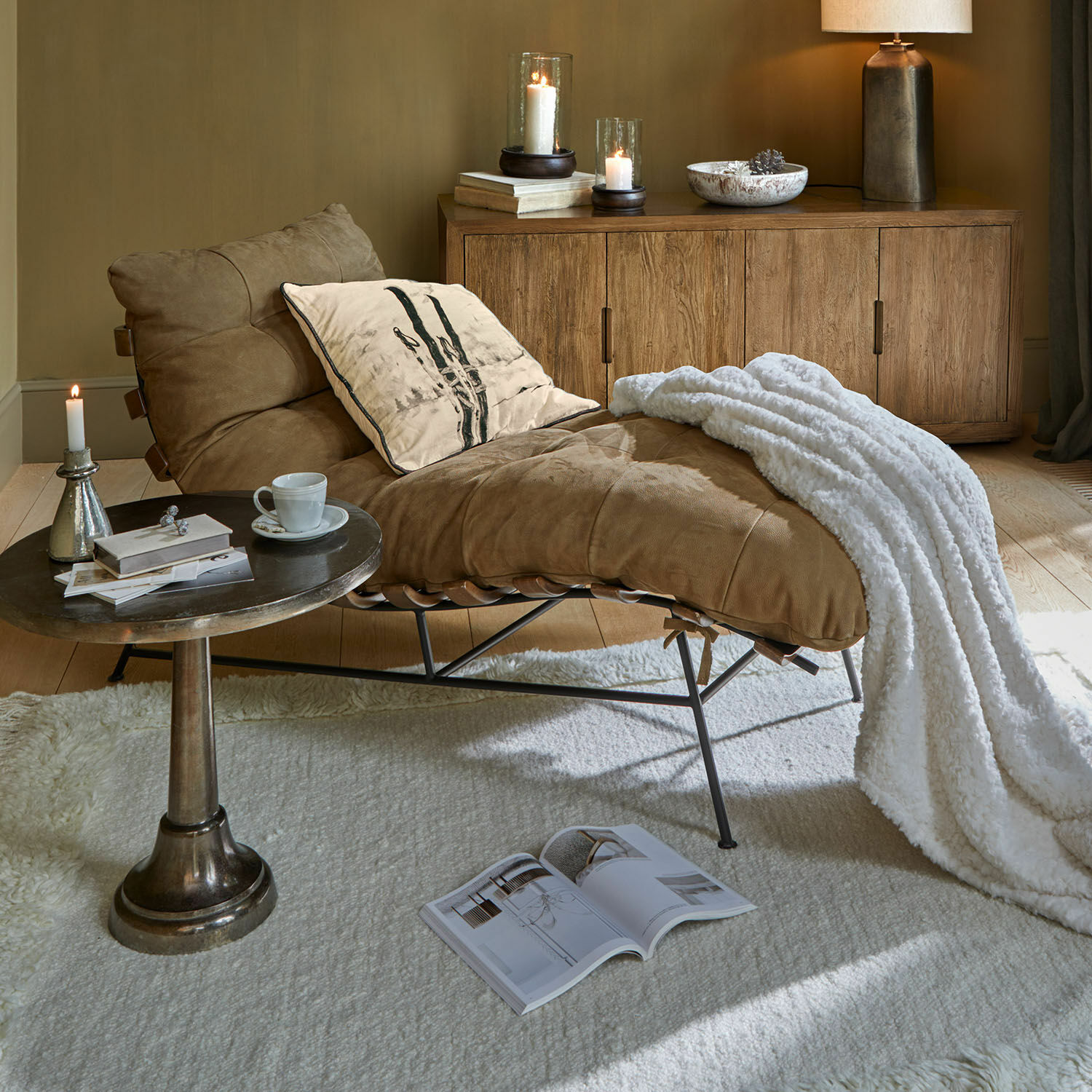 Chaiselongue Horraine Brauner Ledersessel mit weisser Decke und Kissen neben Holzkommode und Beistelltisch im Wohnzimmer