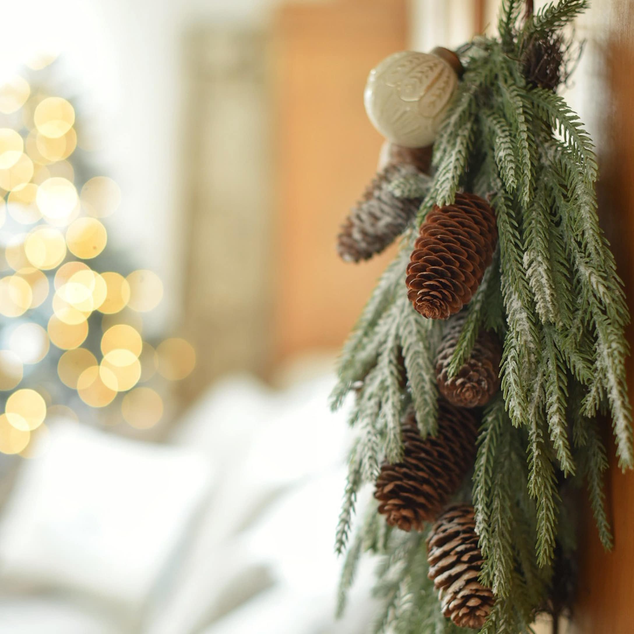 Weihnachtsdekoration mit grünen Zweigen und braunen Zapfen vor unscharfem Lichterhintergrund