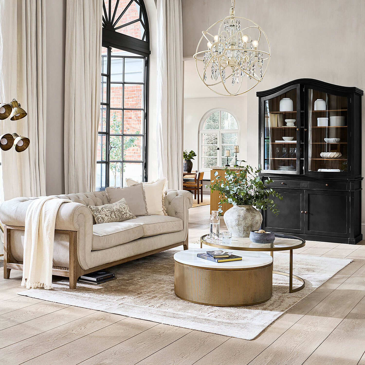 Beige Sofa mit Holzrahmen in hellem Wohnzimmer mit schwarzem Vitrinenschrank und goldenem Couchtisch