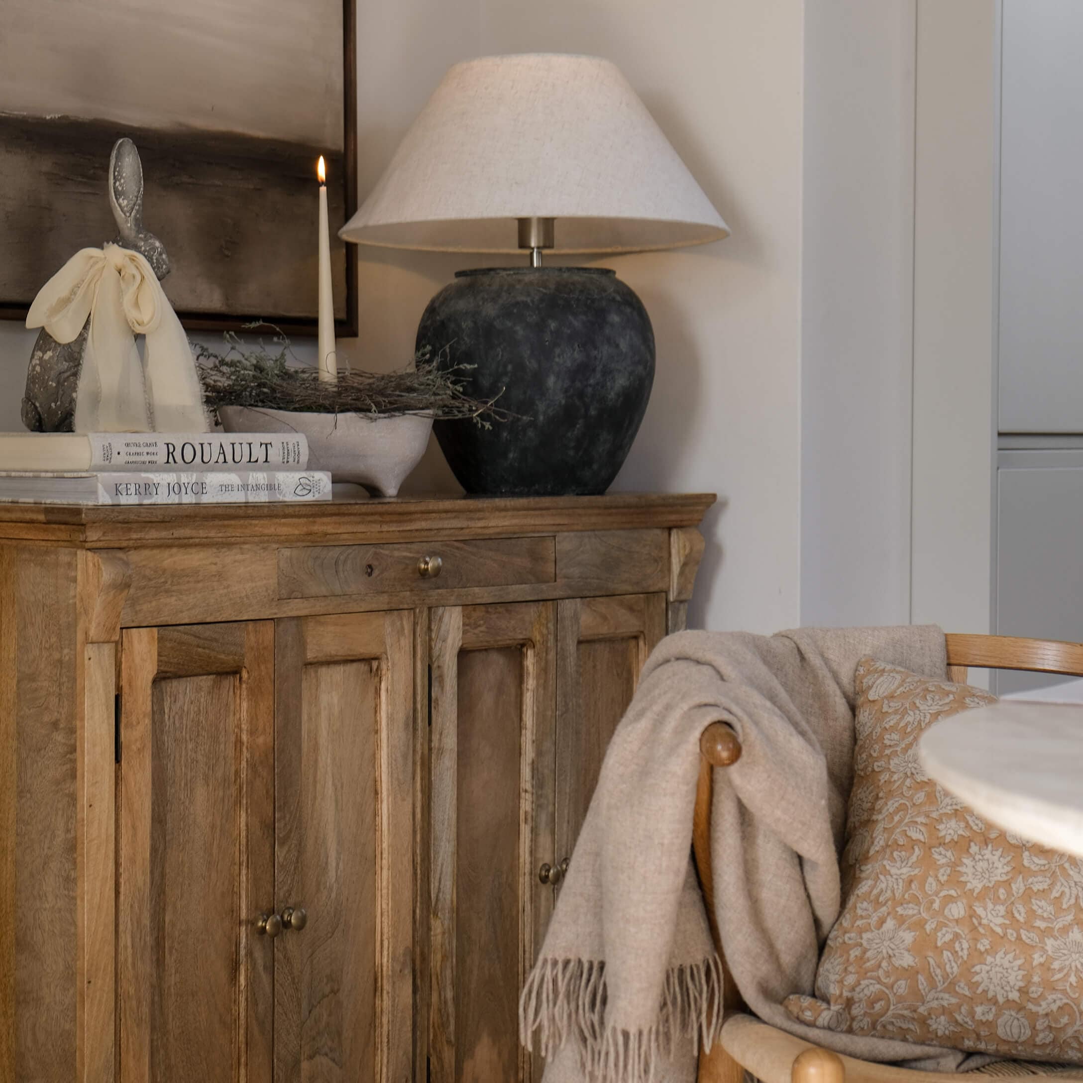 Holzkommode mit Keramiklampe, brennender Kerze und Dekoration in gemütlichem Wohnzimmer