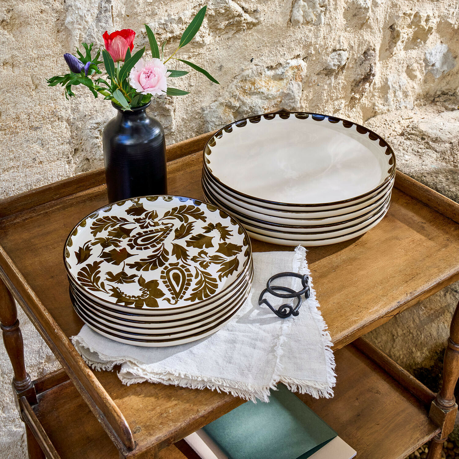 Set aus cremefarbenen Keramiktellern mit braunem Muster auf Holztisch mit schwarzer Vase und Blumen