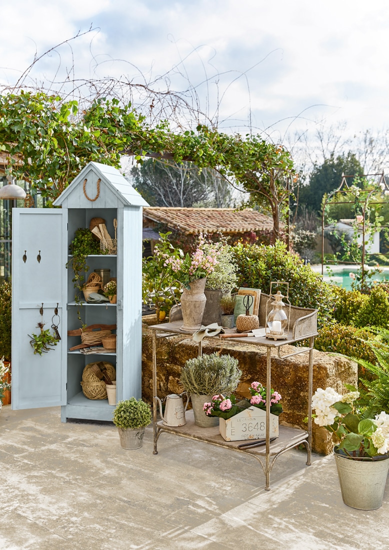 Hellblauer Holz-Gartenschrank mit Regalen und Metalltisch mit Blumen und Gartengeräten im Freien