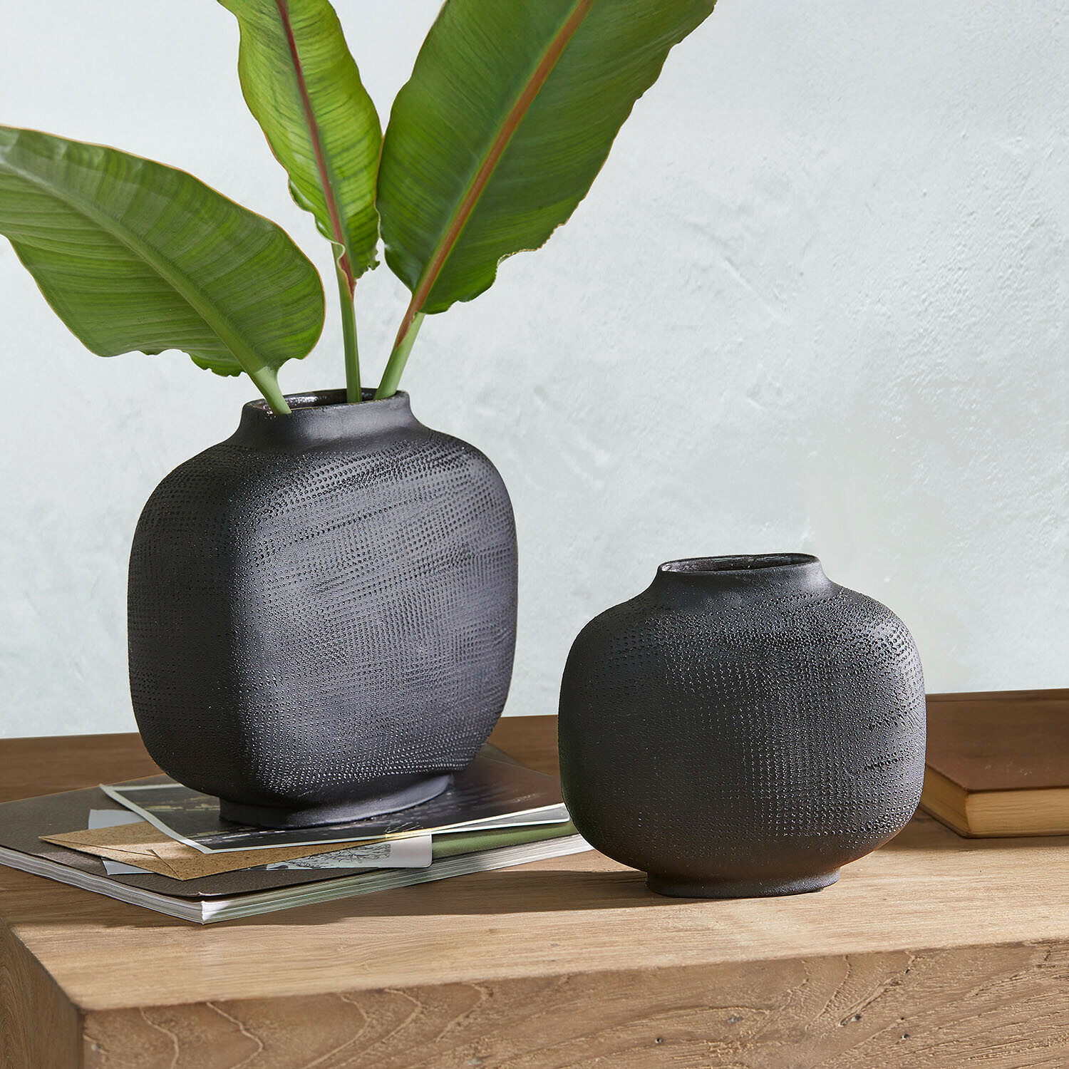 Vase 2er Set Fjordis Zwei schwarze, strukturierte Keramikvasen auf Holztisch mit grünen Blättern und Büchern dekoriert