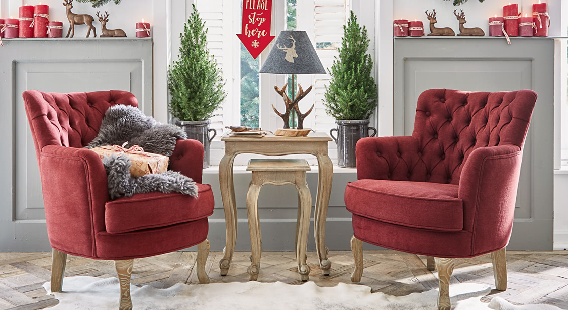 Zwei rote Samt-Sessel mit Holzbeinen neben einem Holztisch und weihnachtlicher Dekoration
