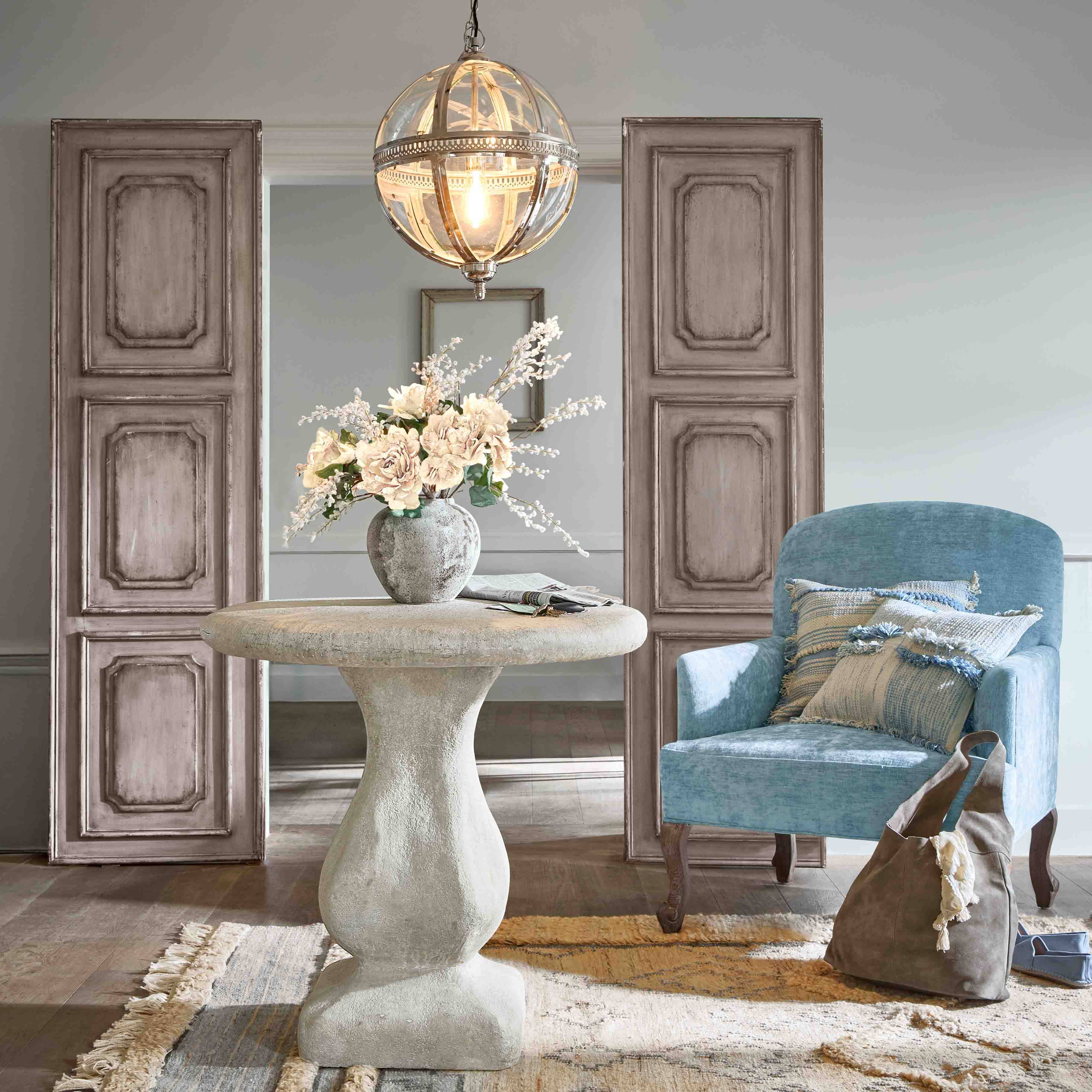 Runder Betontisch mit Blumenvase und blauem Sessel mit Kissen in stilvollem Wohnzimmer