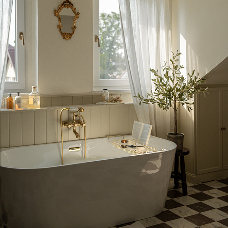 Weisse freistehende Badewanne mit Messingarmatur und dekorativem Spiegel in hellem Badezimmer mit Pflanze