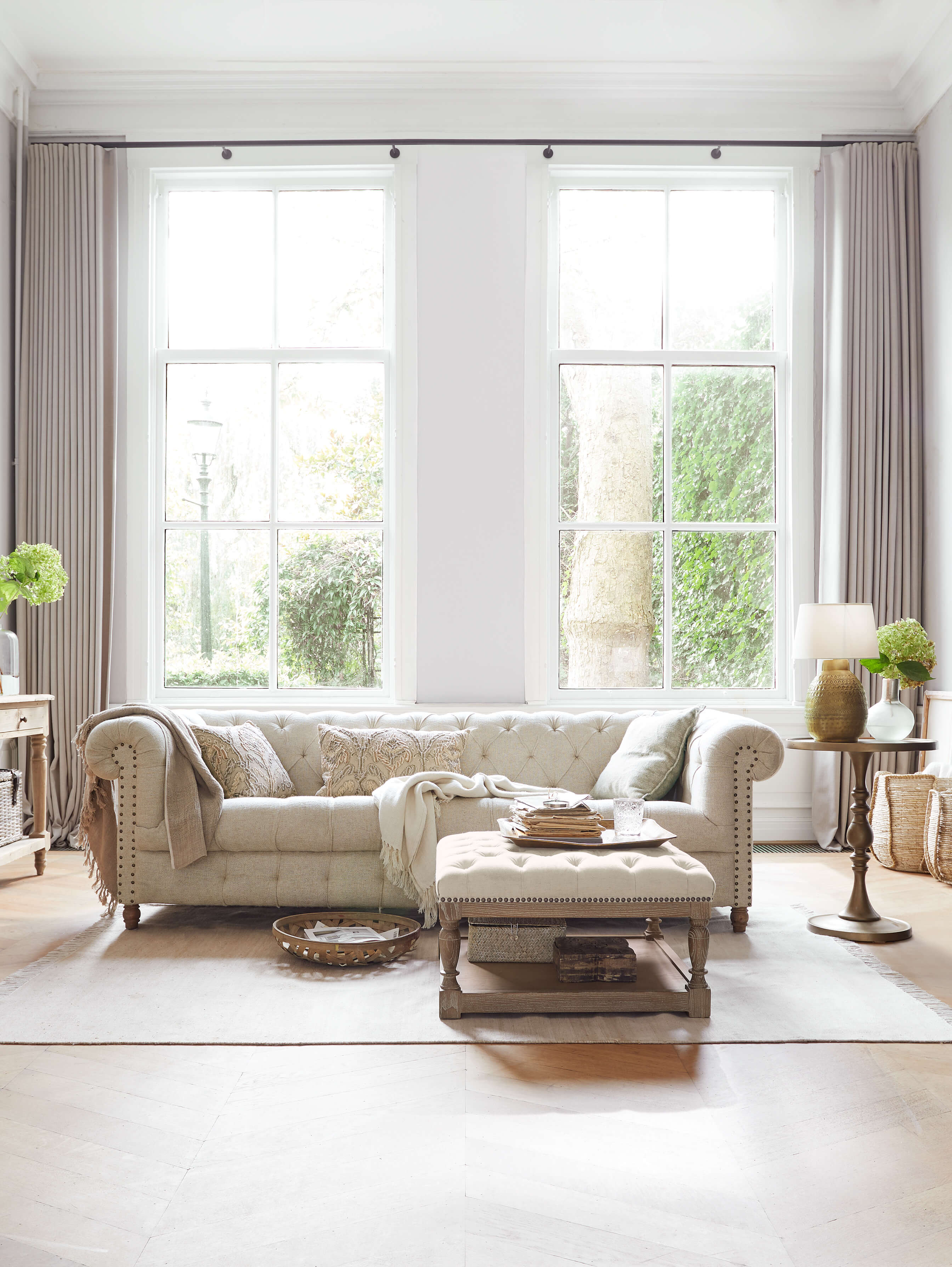 Beiges, gepolstertes Chesterfield-Sofa aus Stoff im hellen Wohnzimmer mit natürlichem Licht