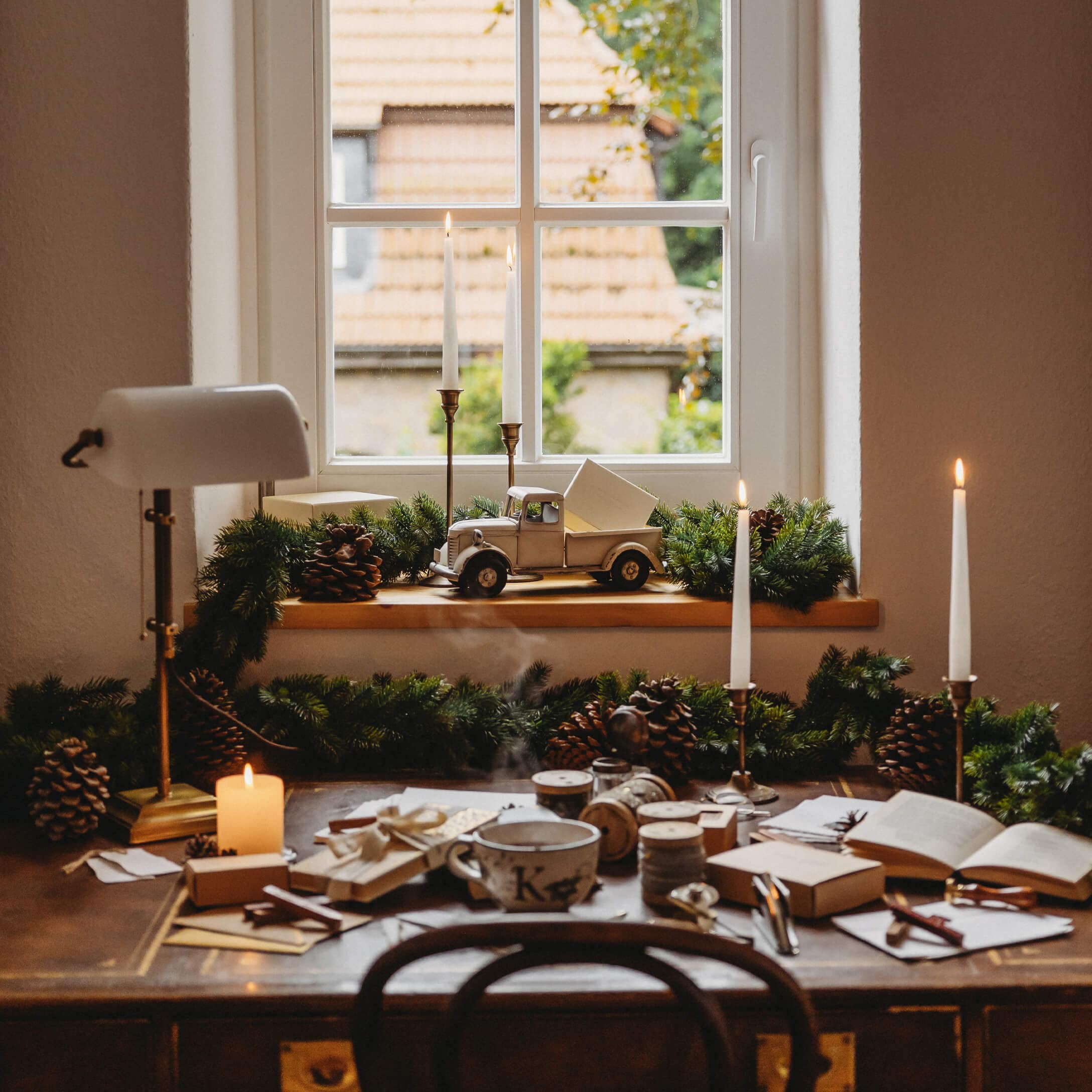 Rustikaler Holztisch mit Weihnachtsdekoration und Kerzen am Fenster mit Blick auf Dachziegeln