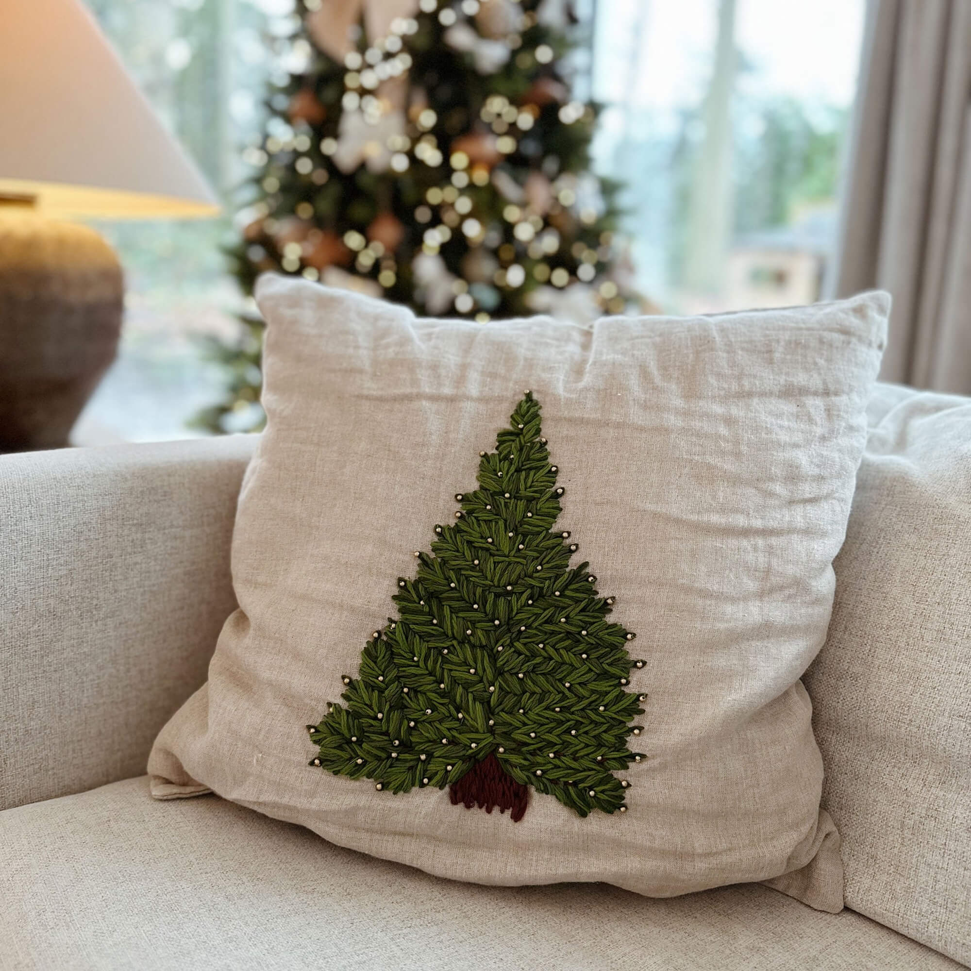 Beiges Leinenkissen mit grünem Tannenbaum-Stickmuster und braunem Stamm auf dem Sofa im Wohnzimmer