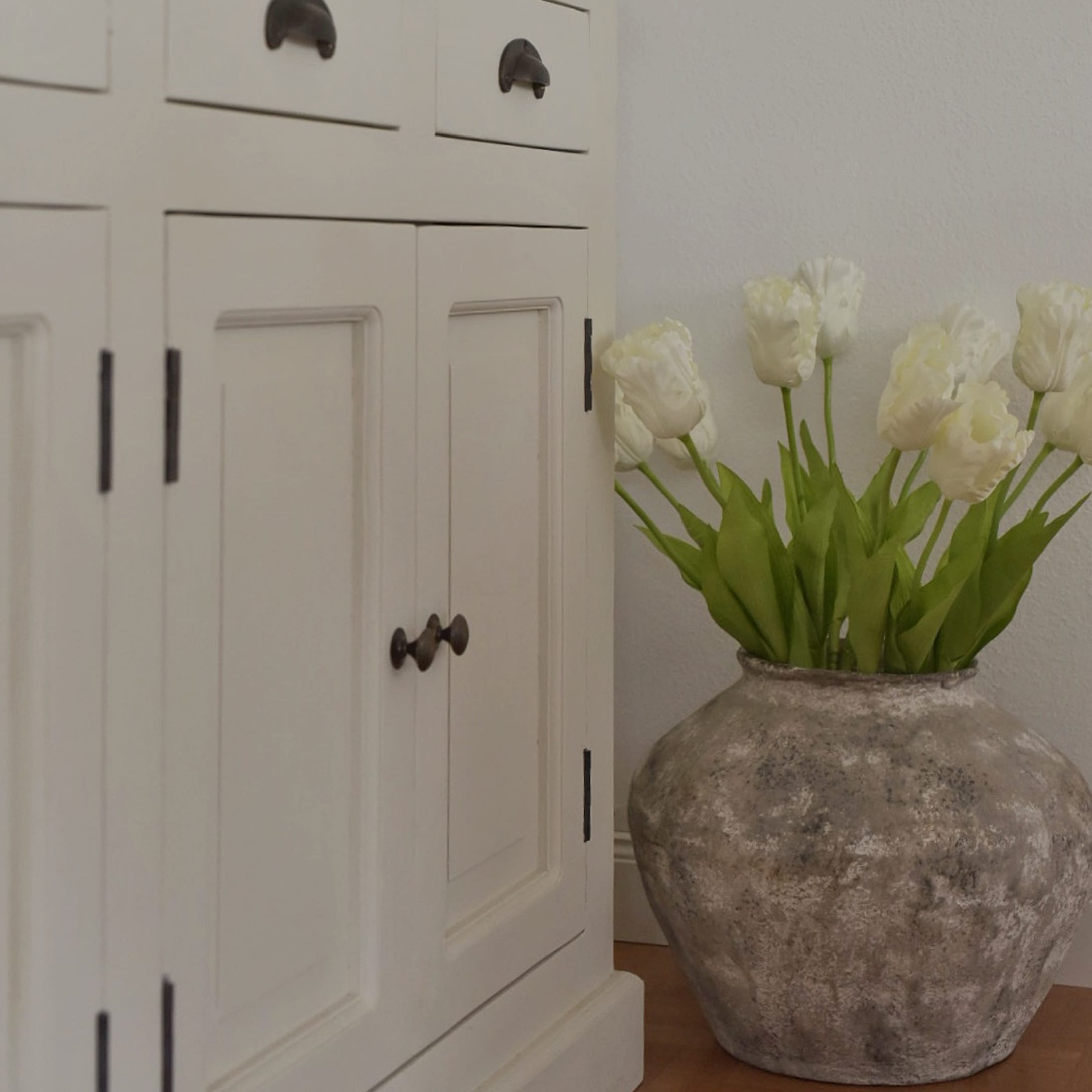 Grosse graue Keramikvase mit weissen Tulpen neben einem weissen Holzschrank