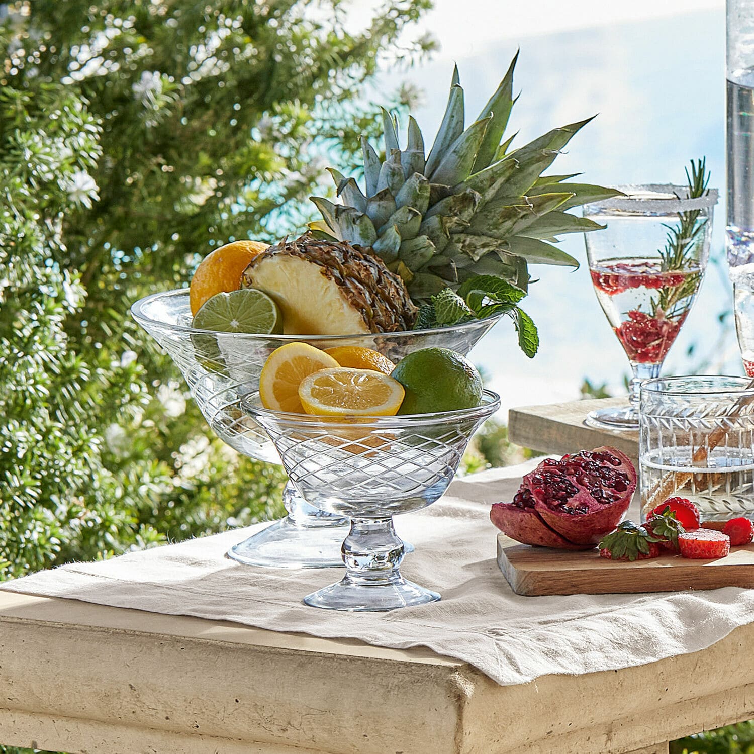 Schalen 2er Set Kadence Glasschalen auf Fuss mit Zitrusfrüchten und Ananas auf hellem Tisch im Freien